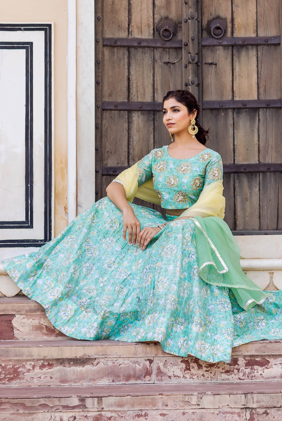 Model sitting wearing an aqua green hand block printed floral embroidered lehenga set.