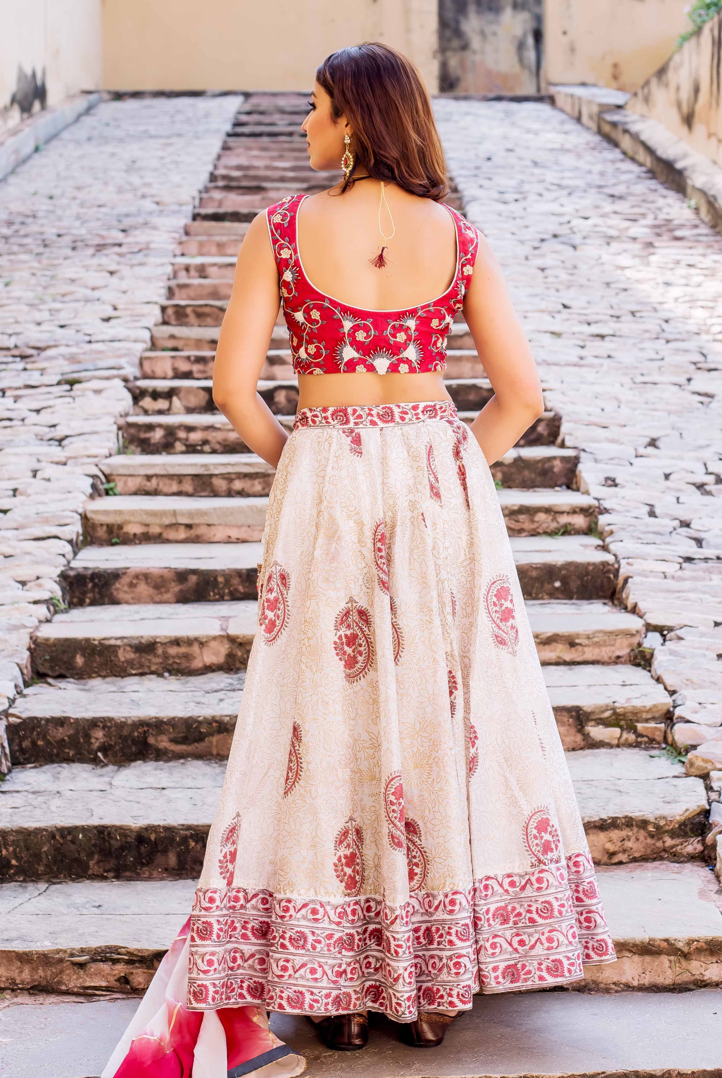 Back view of model in red embroidered blouse and cream hand-block printed lehenga.