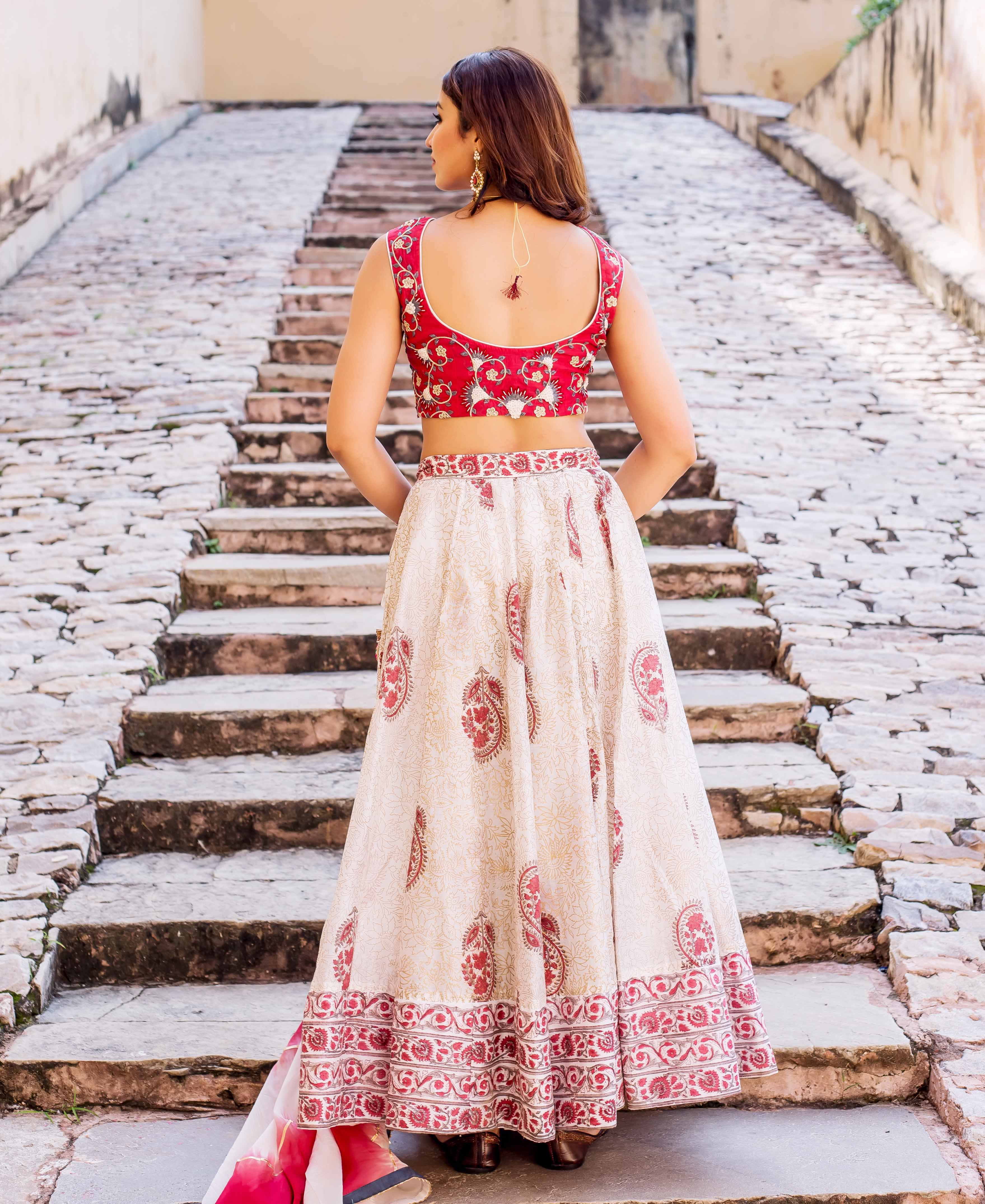 Back view of model in red embroidered blouse and cream hand-block printed lehenga.