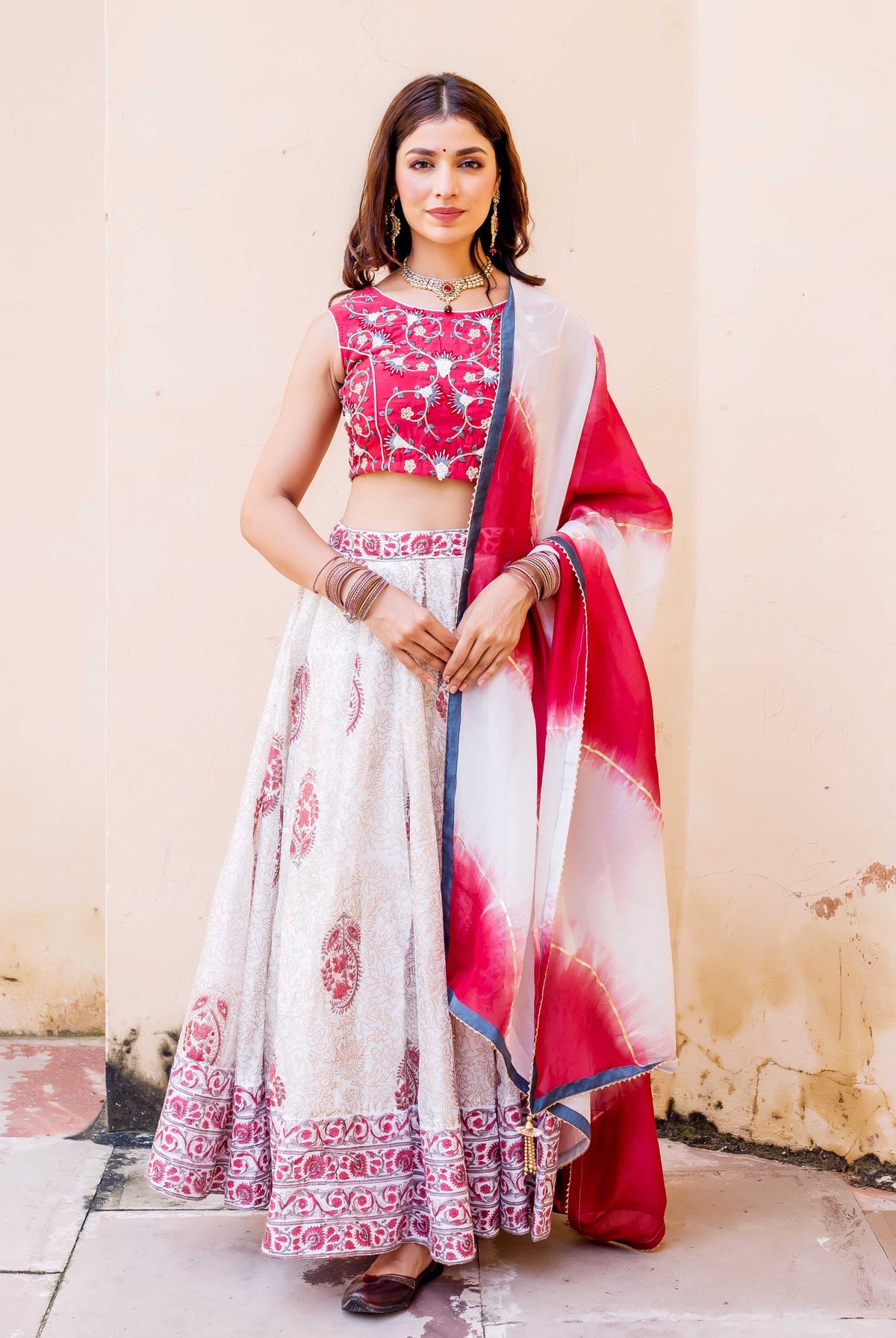 Woman posing in full-length white and red hand-block printed lehenga set with embroidery.