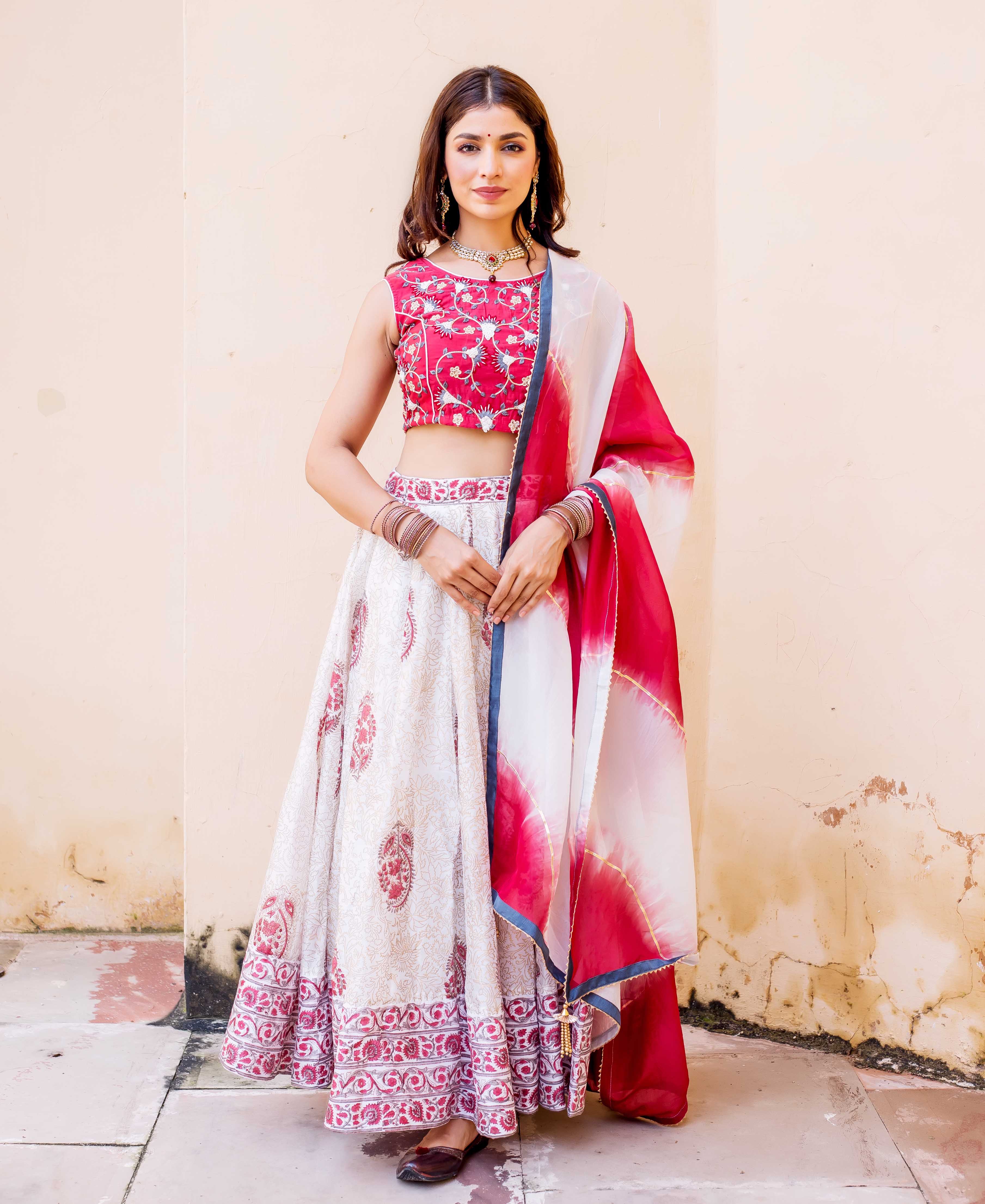 Woman posing in full-length white and red hand-block printed lehenga set with embroidery.
