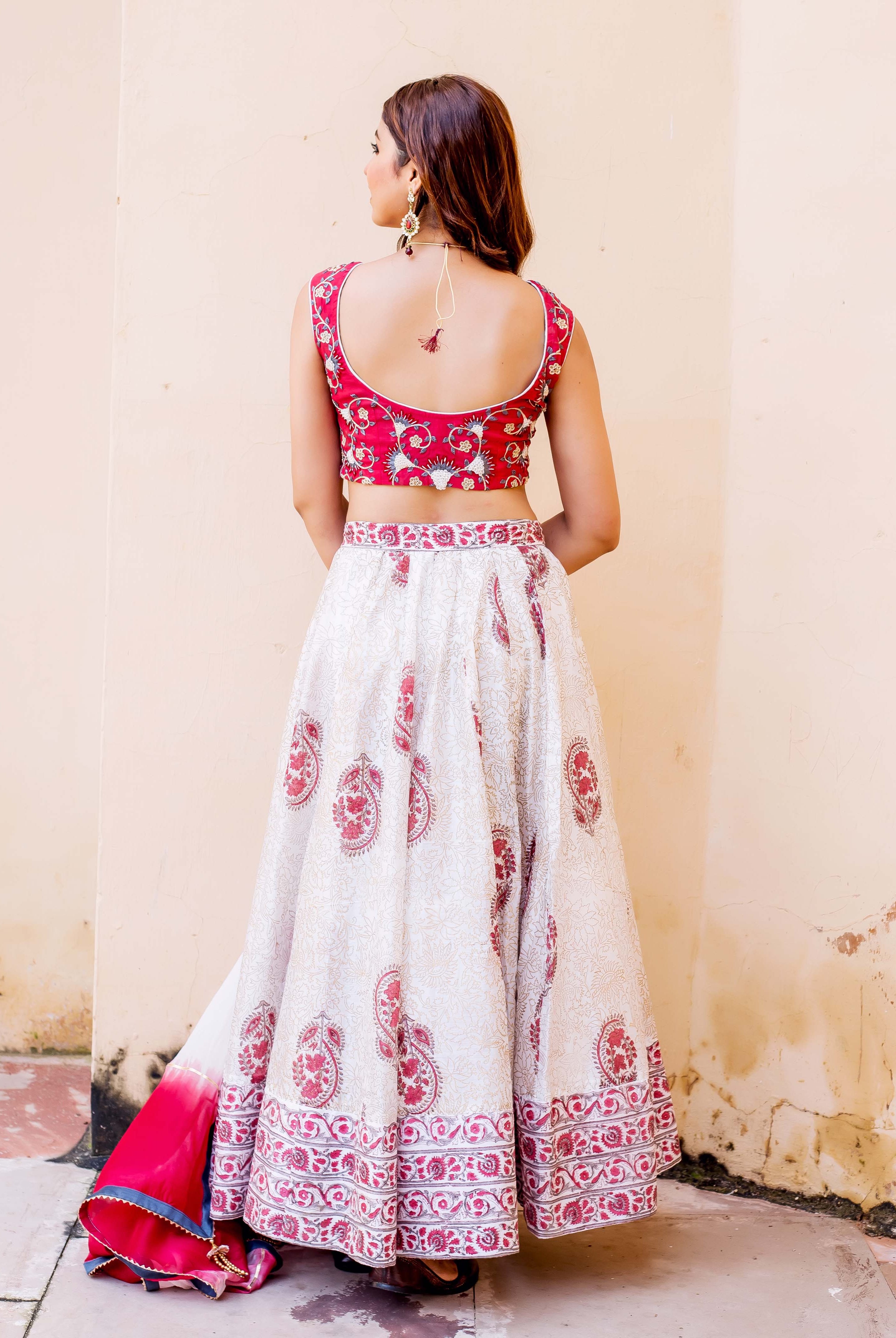 Back view of model in red embroidered, white hand-block printed lehenga set with paisley designs.
