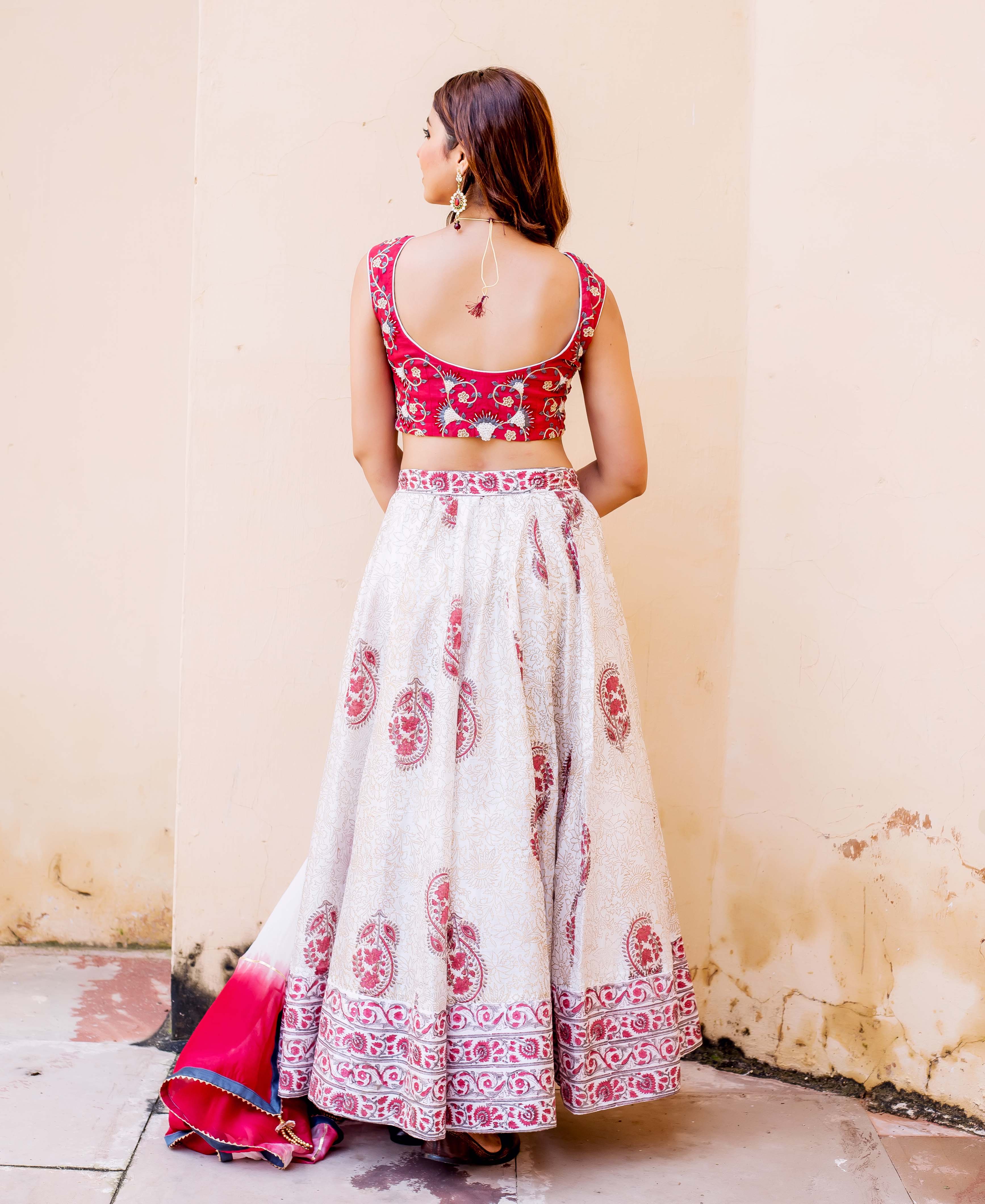 Back view of model in red embroidered, white hand-block printed lehenga set with paisley designs.