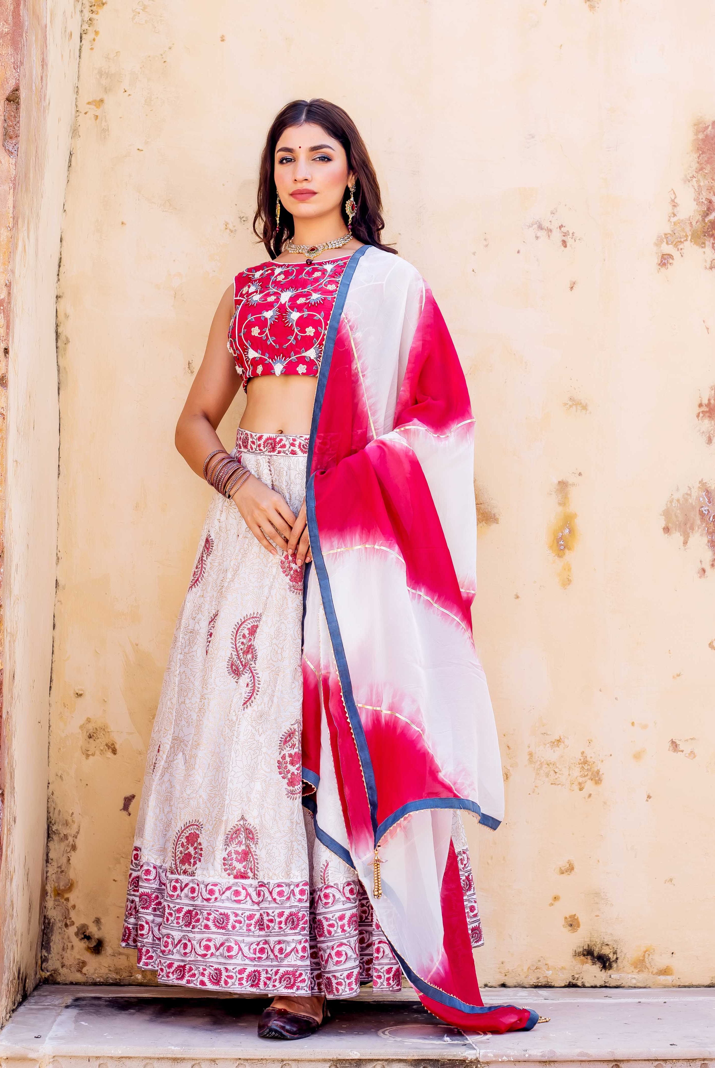 Woman models red embroidered blouse, cream hand-block printed lehenga, and white-red tie-dye dupatta.