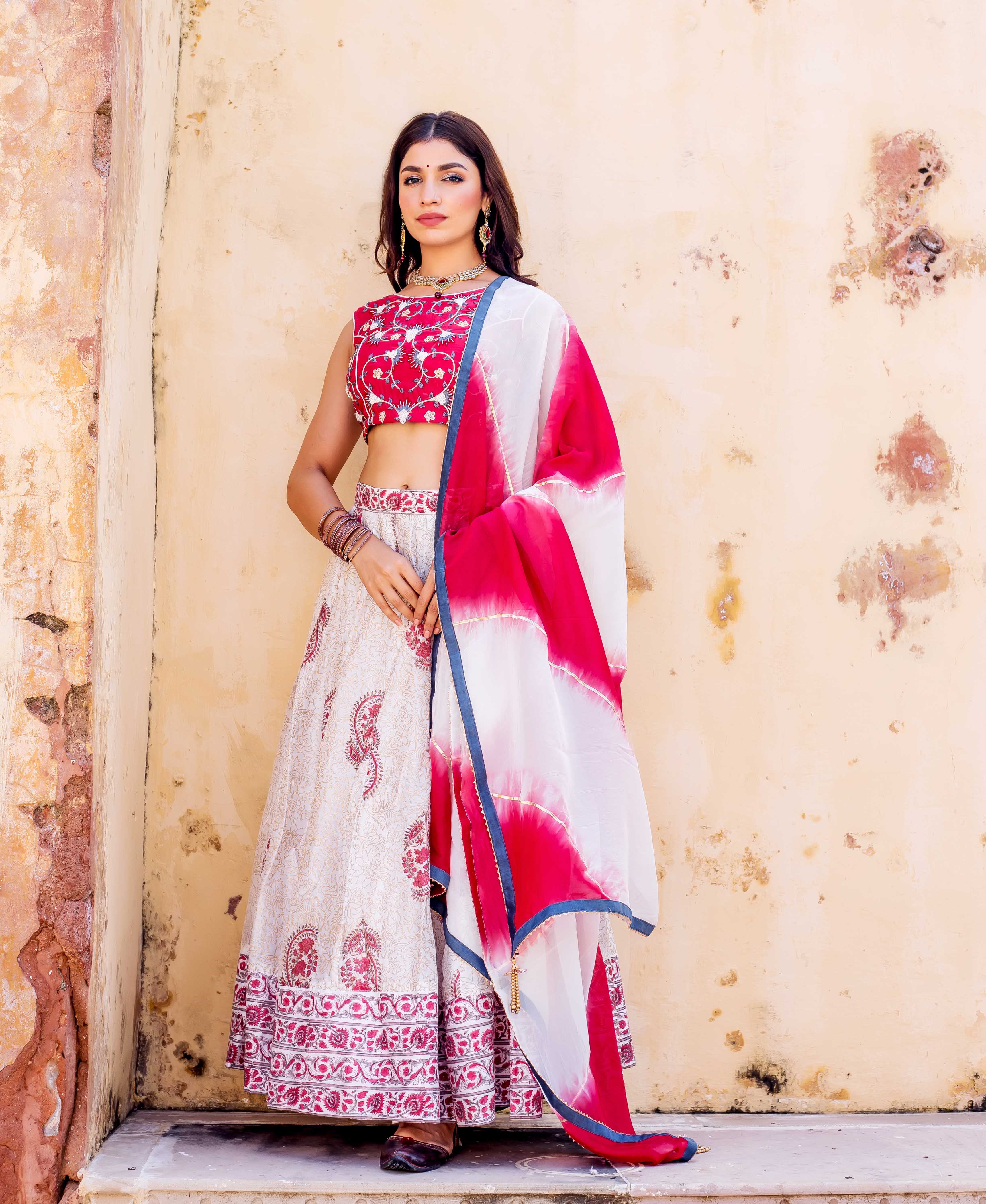 Woman models red embroidered blouse, cream hand-block printed lehenga, and white-red tie-dye dupatta.