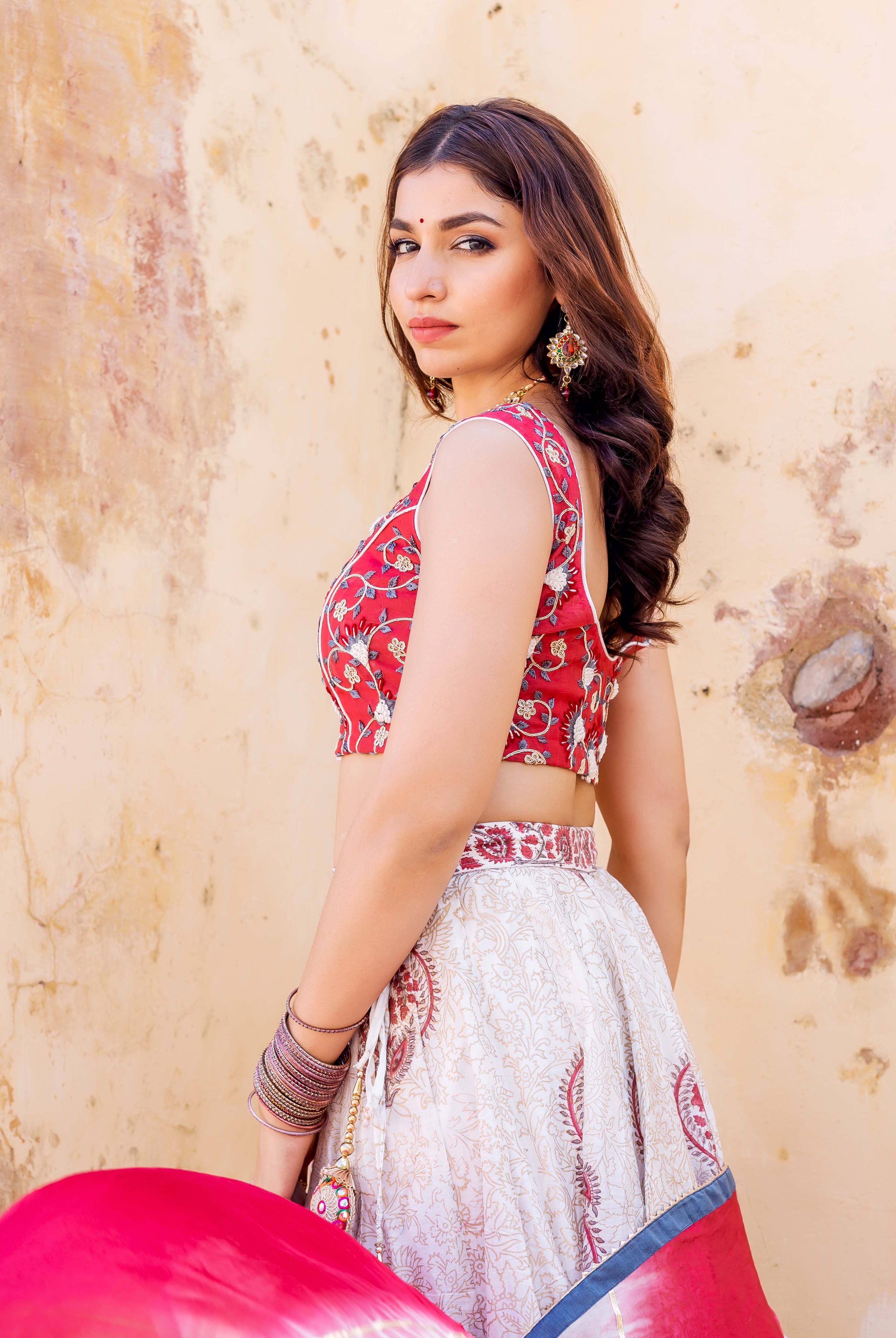 Model in red embroidered crop top and off-white hand block printed lehenga set.
