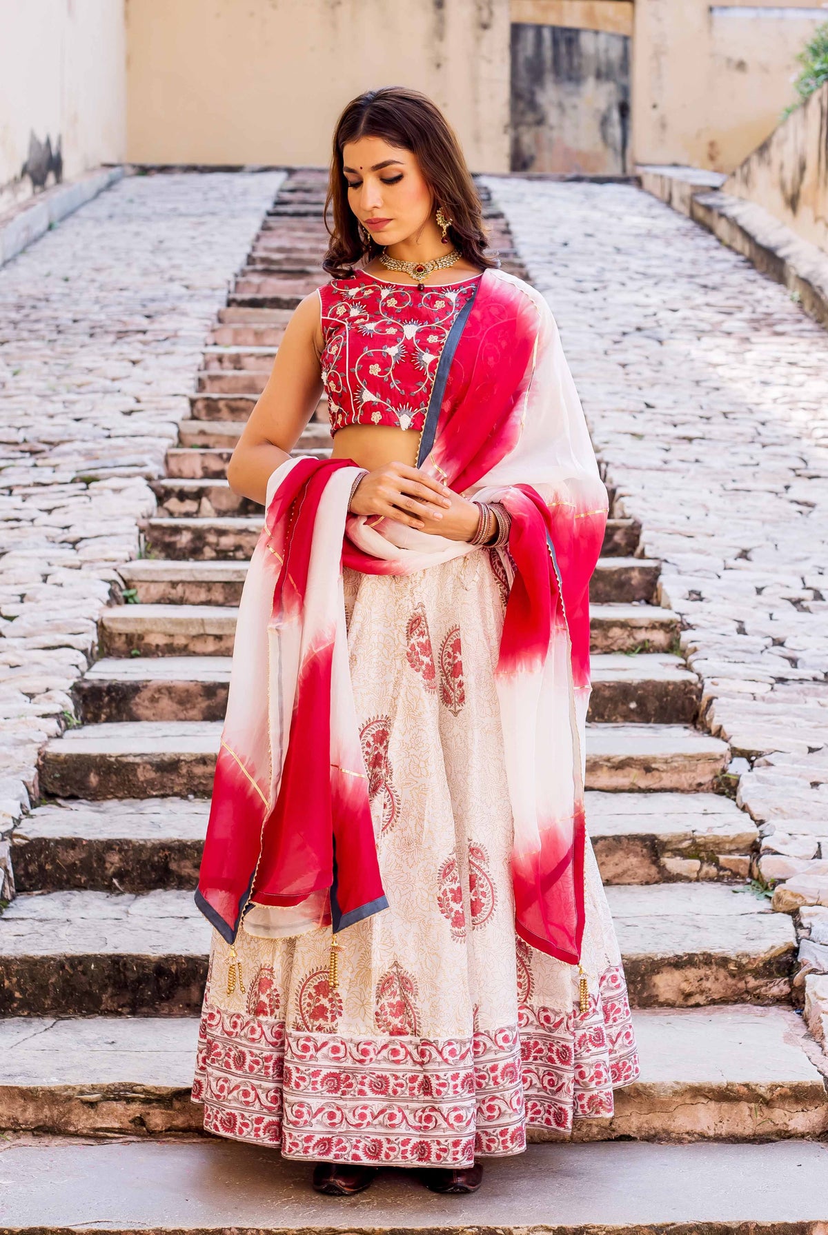 Woman models cream hand-block printed lehenga with red embroidered top and tie-dye dupatta.