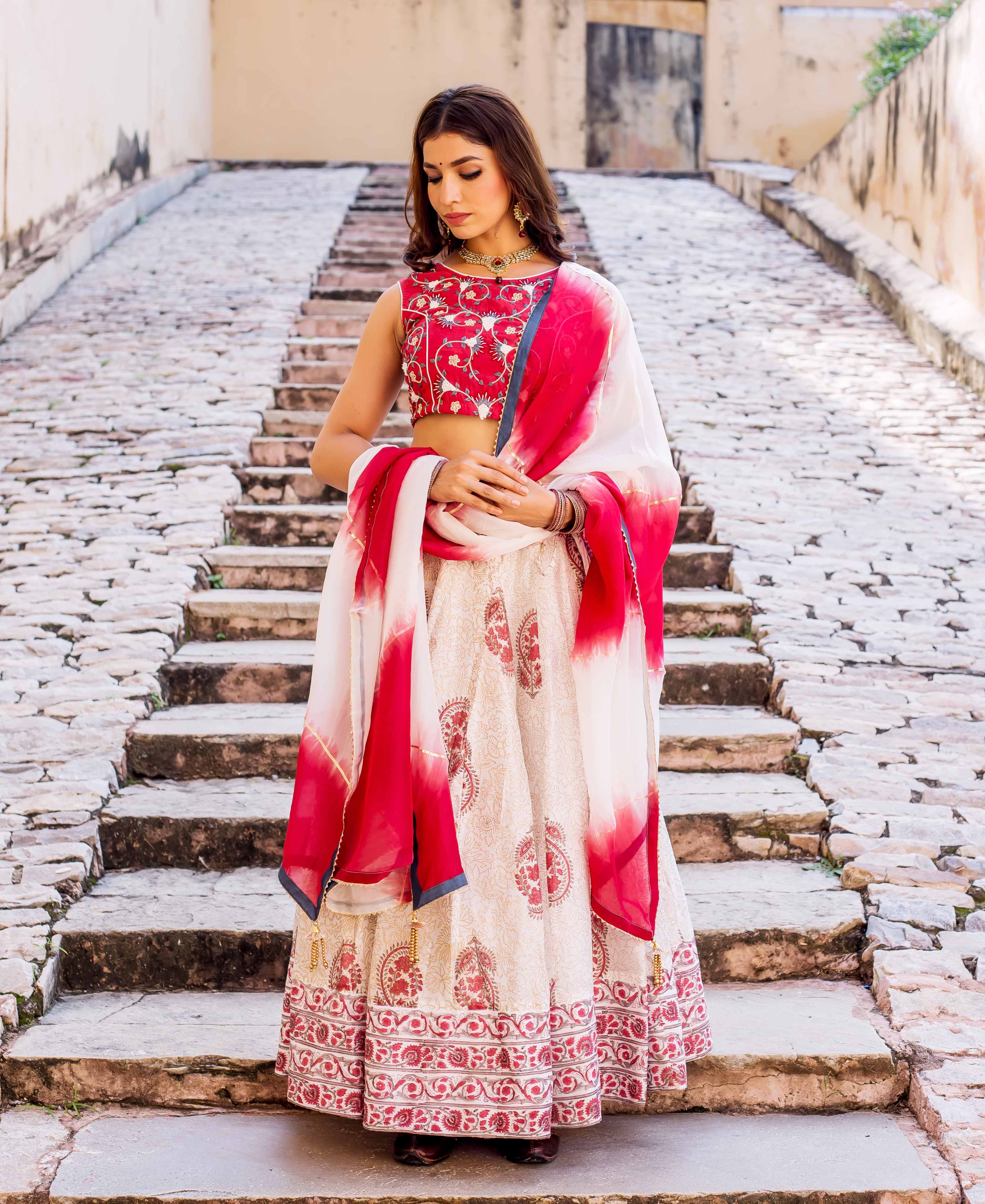 Woman models cream hand-block printed lehenga with red embroidered top and tie-dye dupatta.