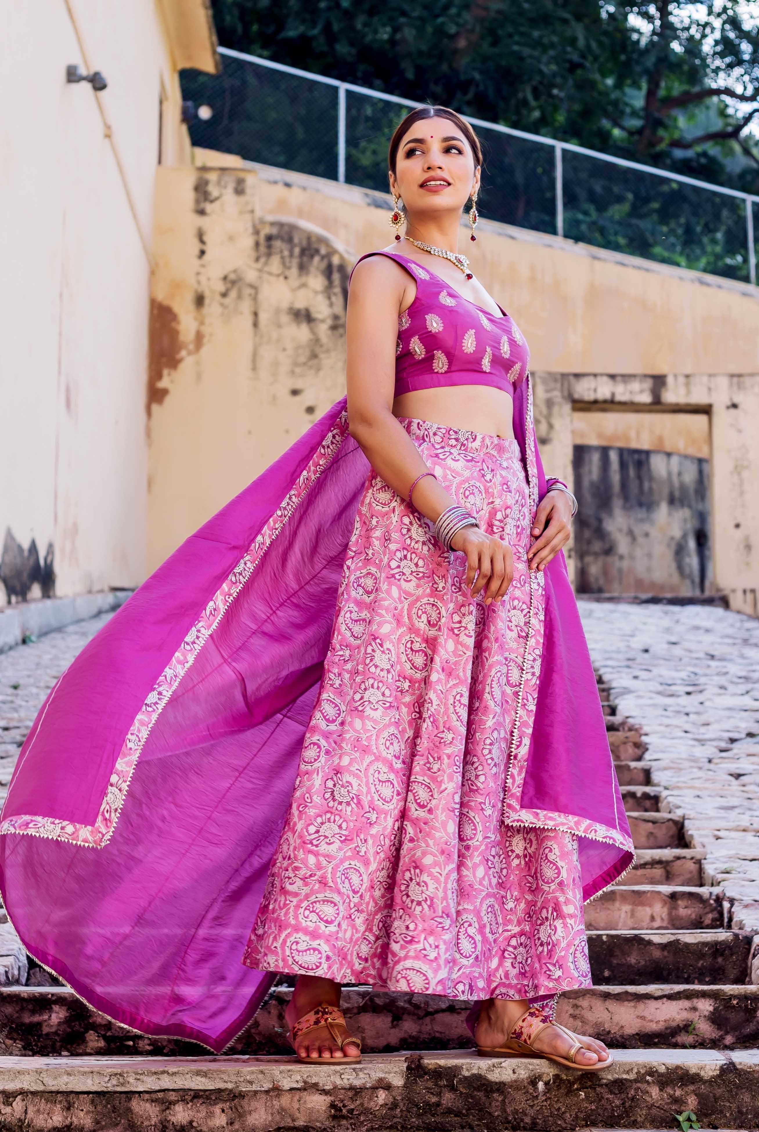 Model in a full pink and purple hand block printed lehenga set with a flowing dupatta.