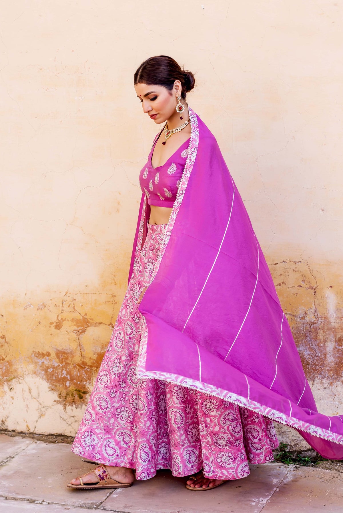 Side view of model in pink hand-block-printed lehenga set with a purple striped dupatta.