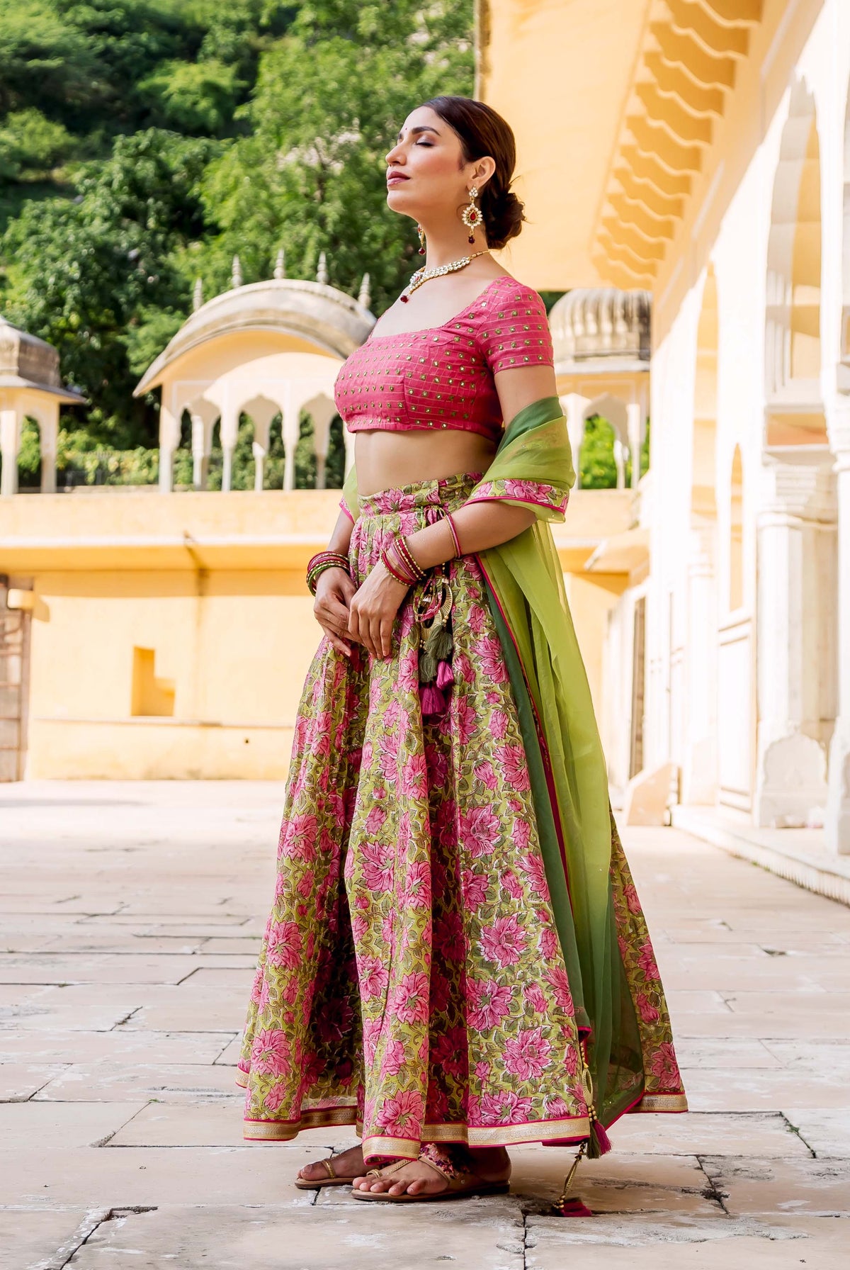 Side view of model wearing a pink embroidered blouse and green floral block printed lehenga set.