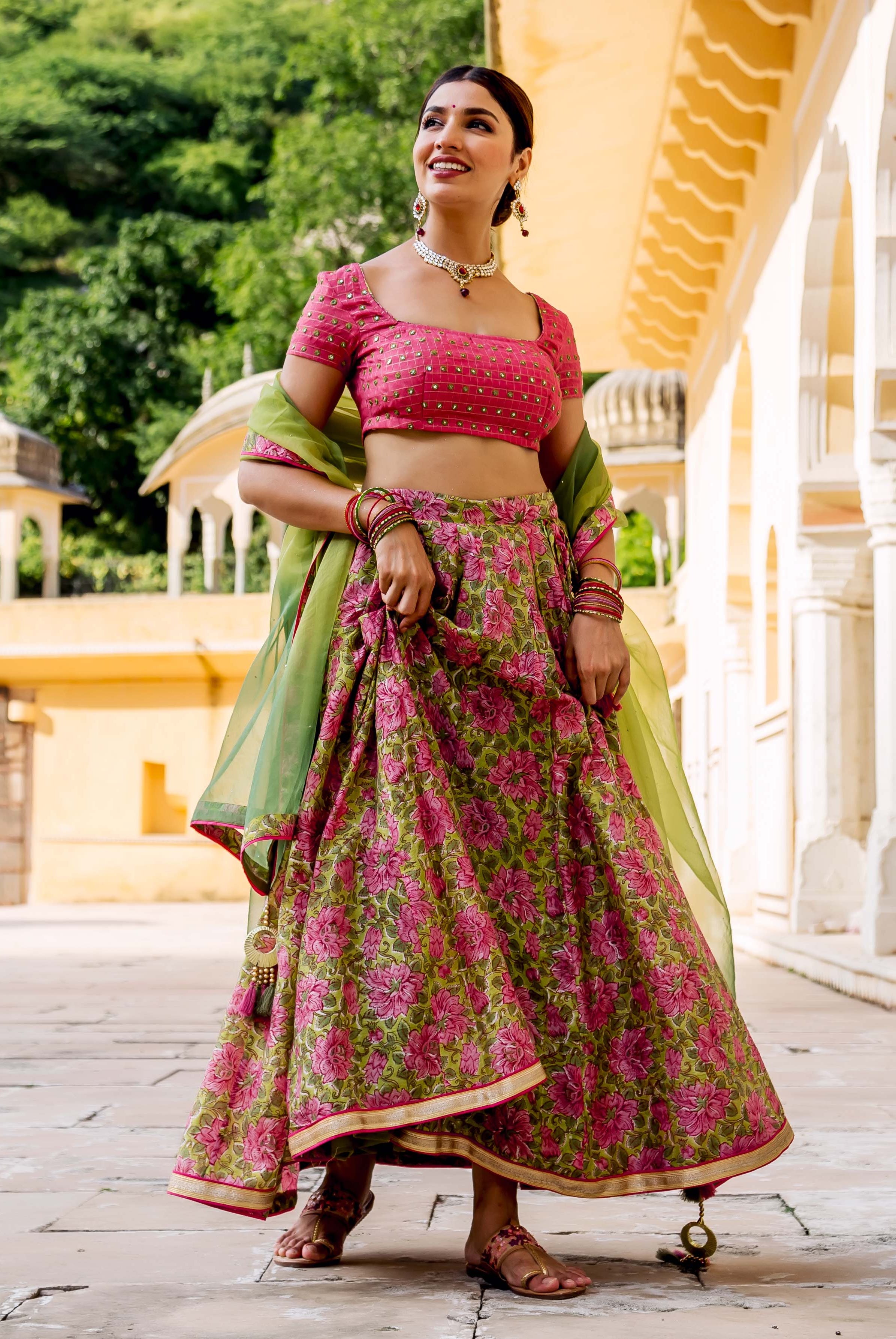 A model wearing a pink and green floral lehenga set with embroidery.