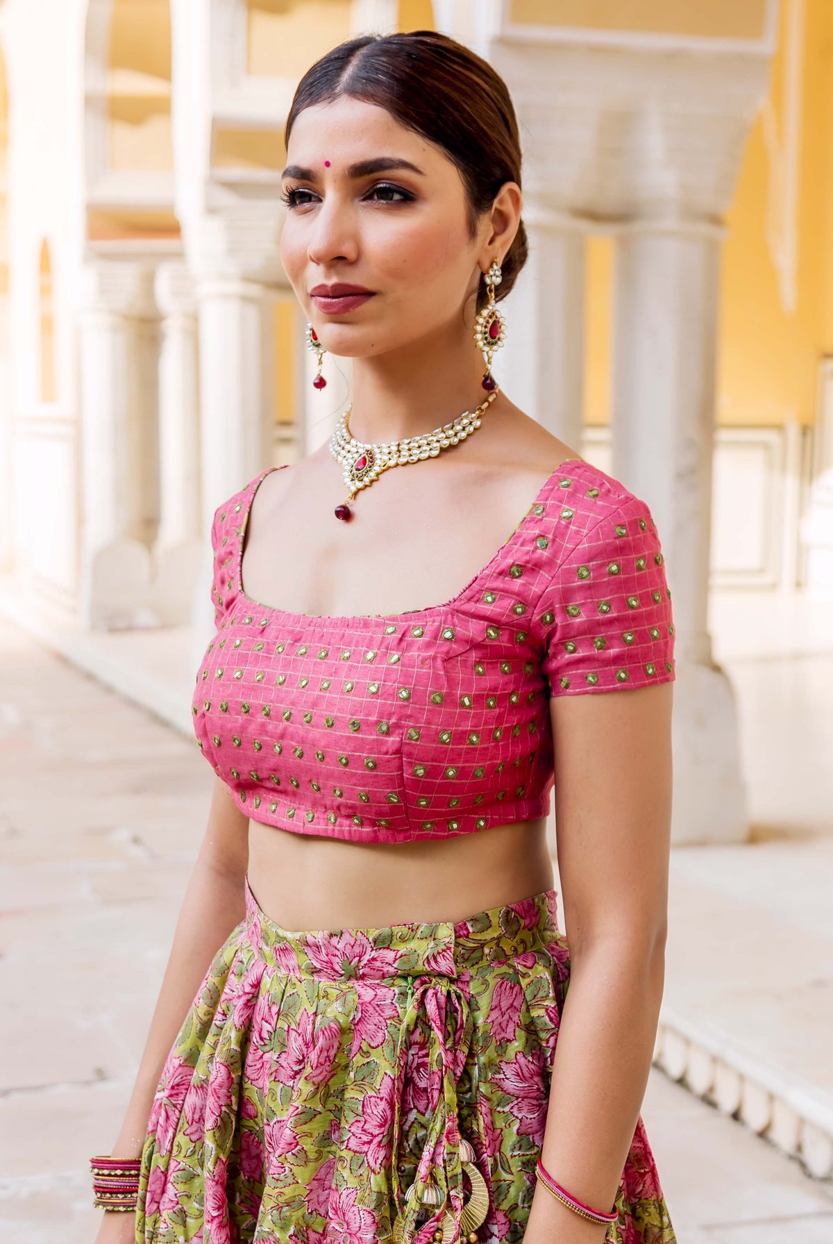 Model in vibrant pink embroidered top and green floral block print lehenga skirt.