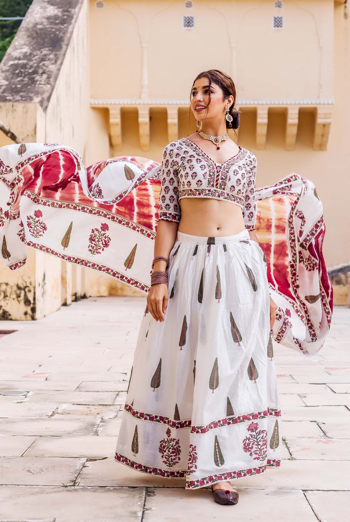 Smiling model in white hand-block printed lehenga set with maroon and green motifs, dupatta flying.
