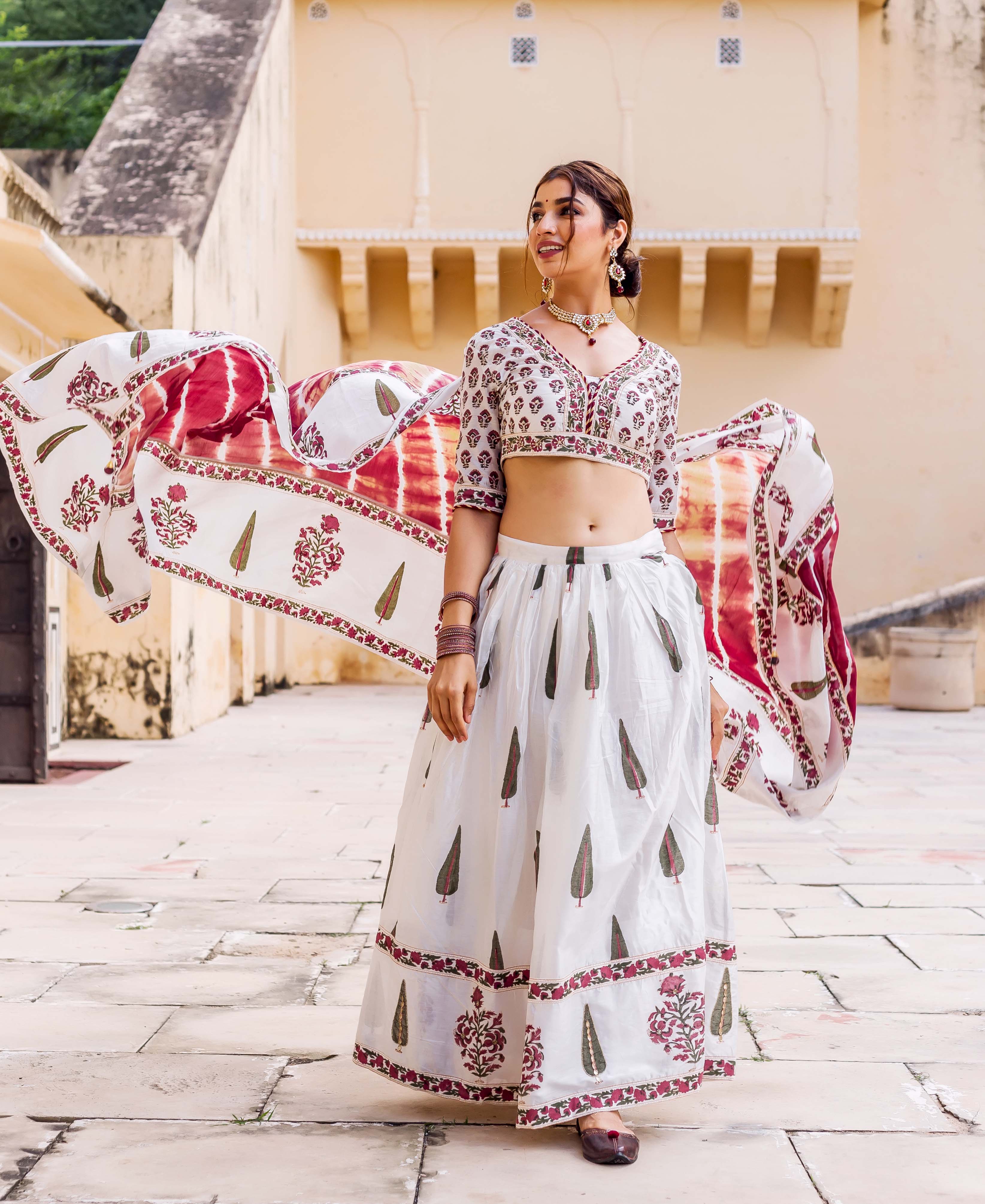 Smiling model in white hand-block printed lehenga set with maroon and green motifs, dupatta flying.