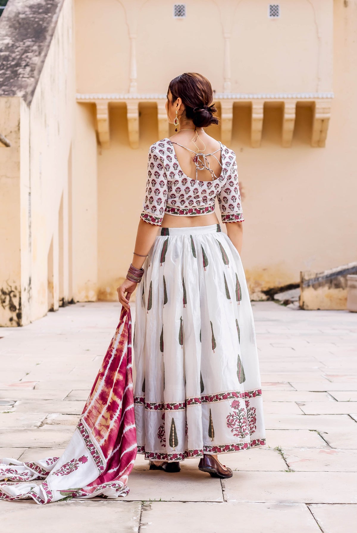 Back view of woman wearing white hand-block printed lehenga set with maroon and green motifs.