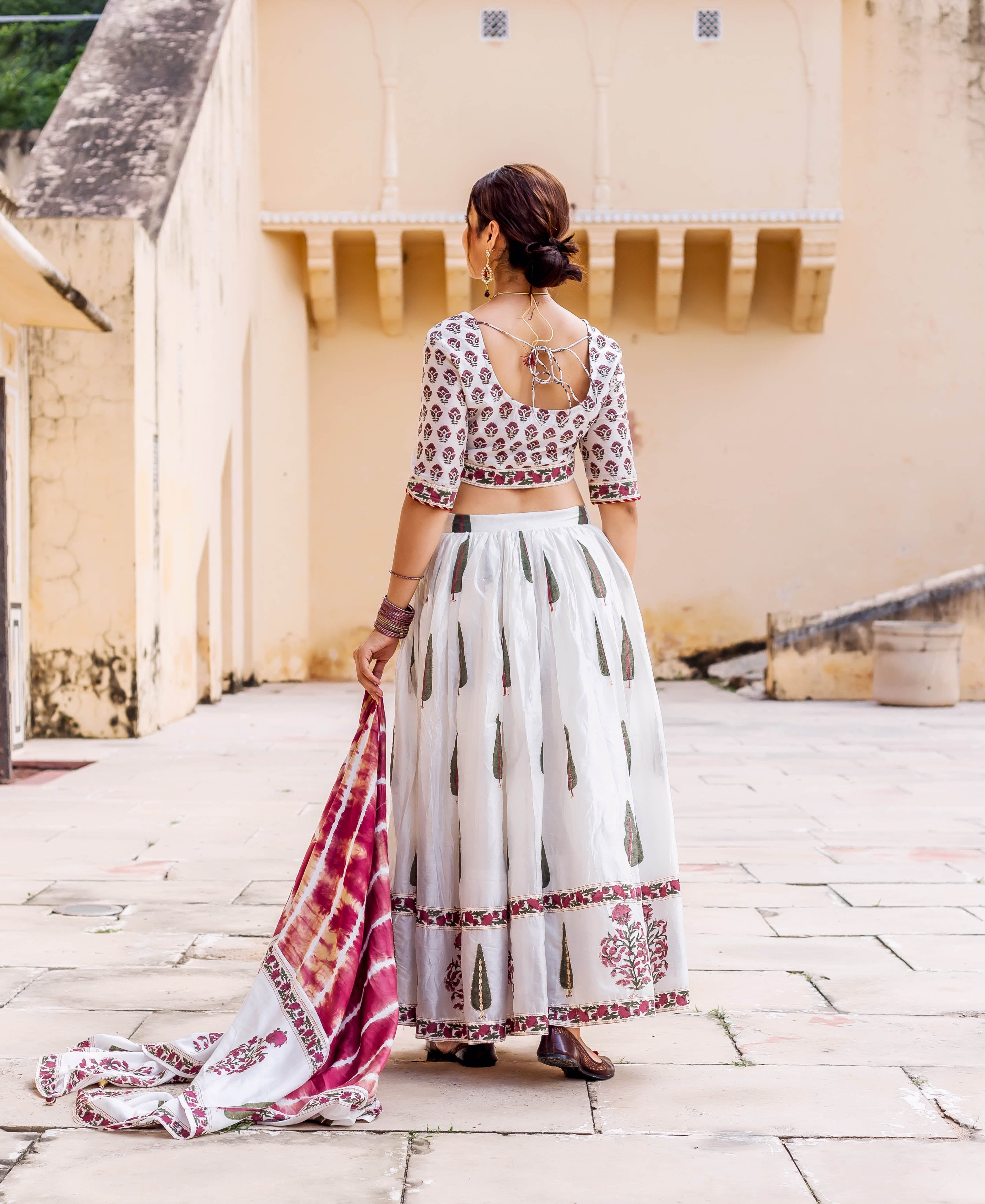 Back view of woman wearing white hand-block printed lehenga set with maroon and green motifs.