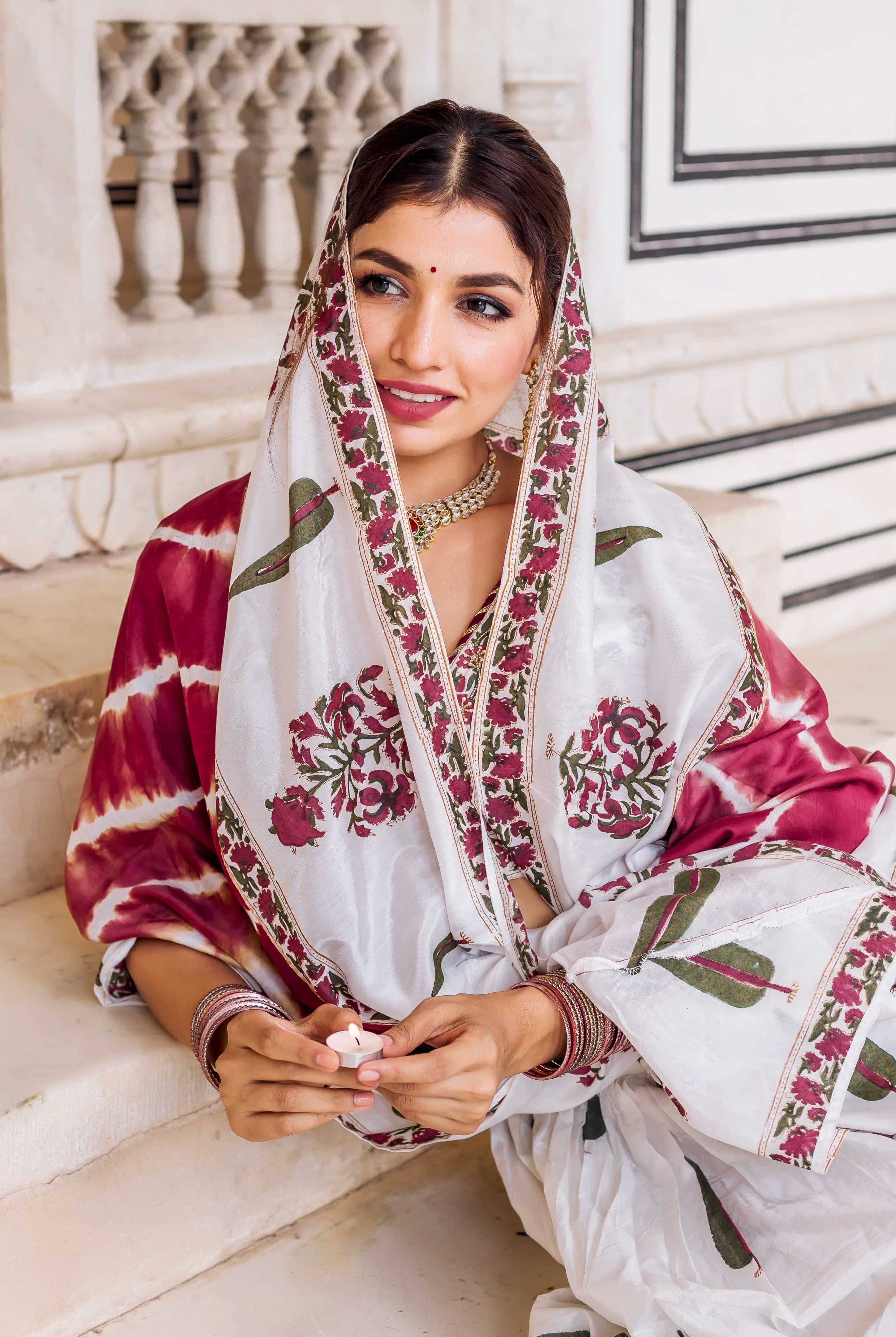 Model seated, wearing a white and maroon hand-block printed lehenga set with floral and tie-dye patterns.