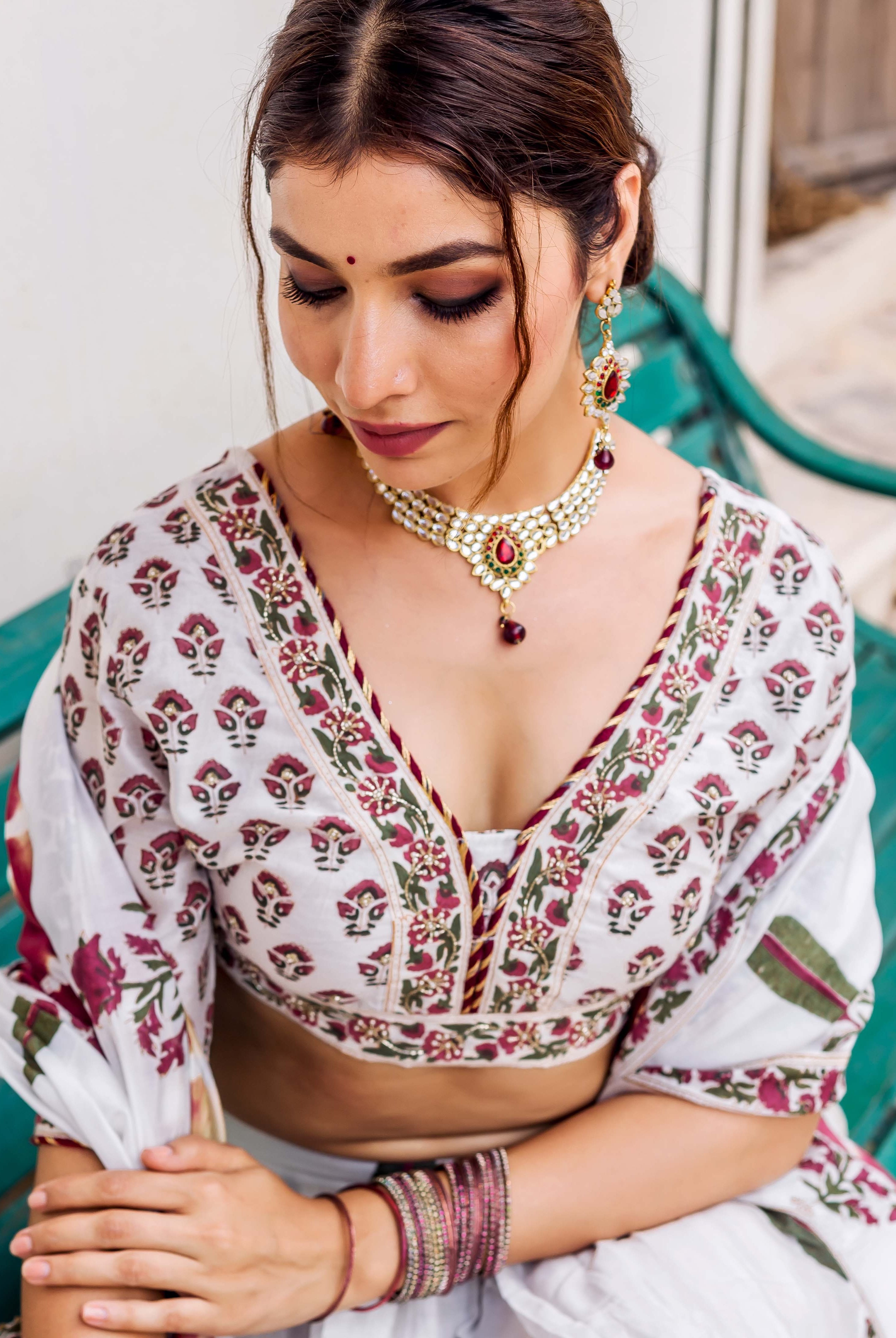 Model sitting, looking down, wearing white hand-block printed blouse with maroon and green floral patterns.
