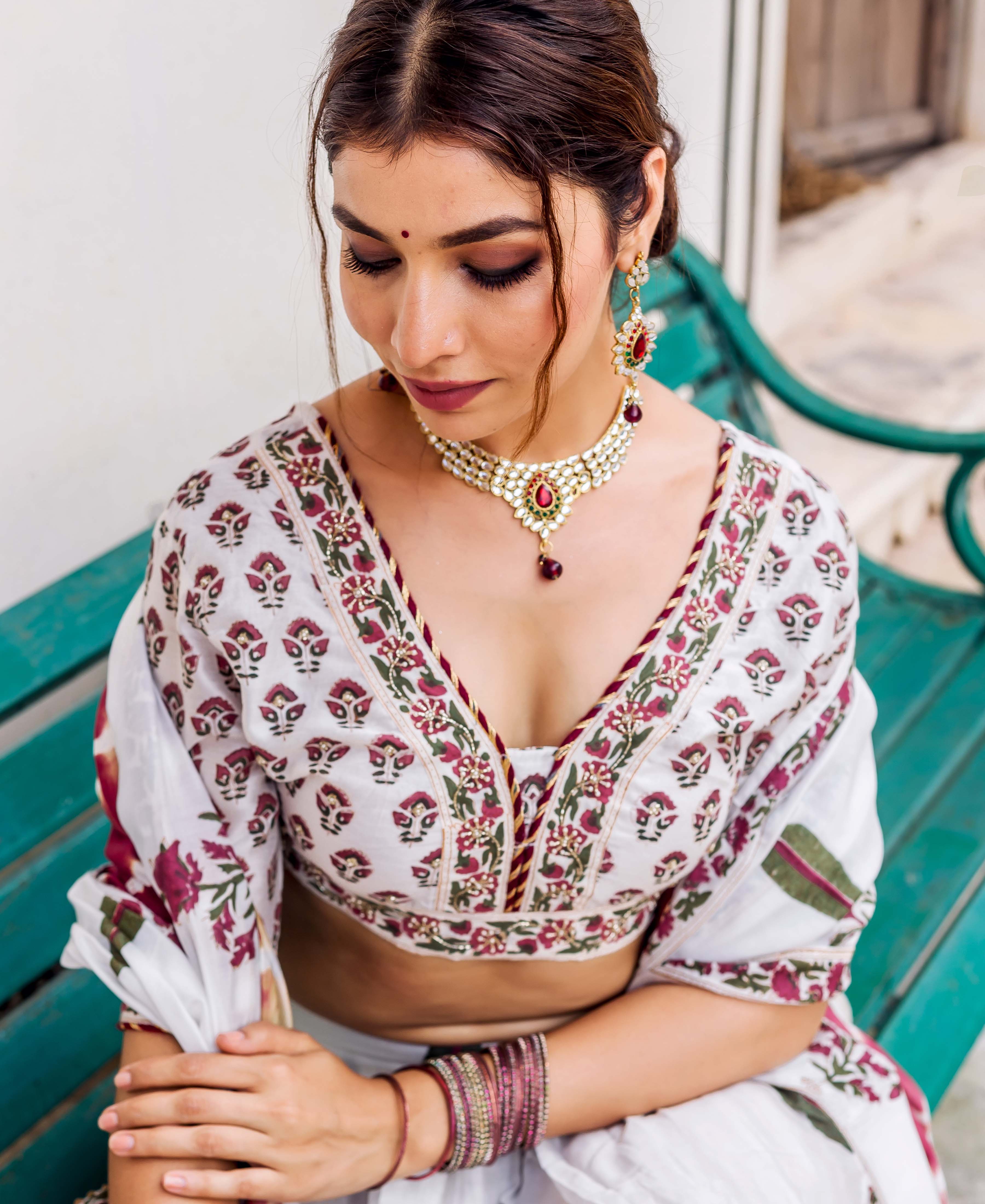 Model sitting, looking down, wearing white hand-block printed blouse with maroon and green floral patterns.
