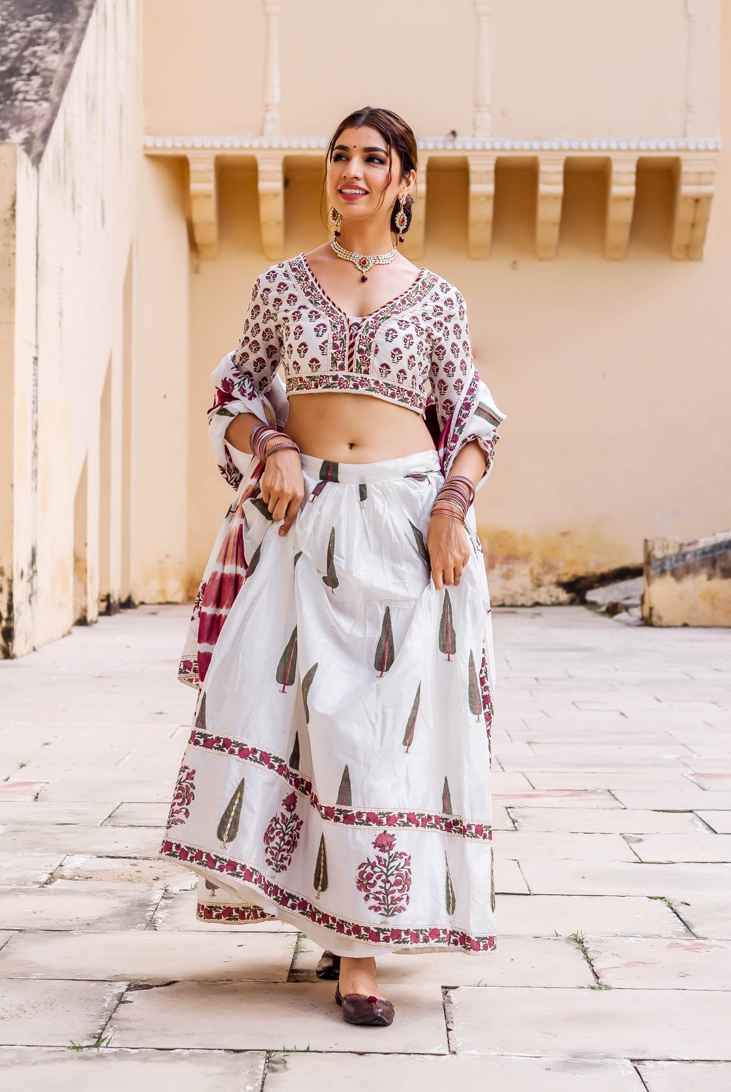Smiling model in white hand-block printed lehenga set with maroon and green patterns.