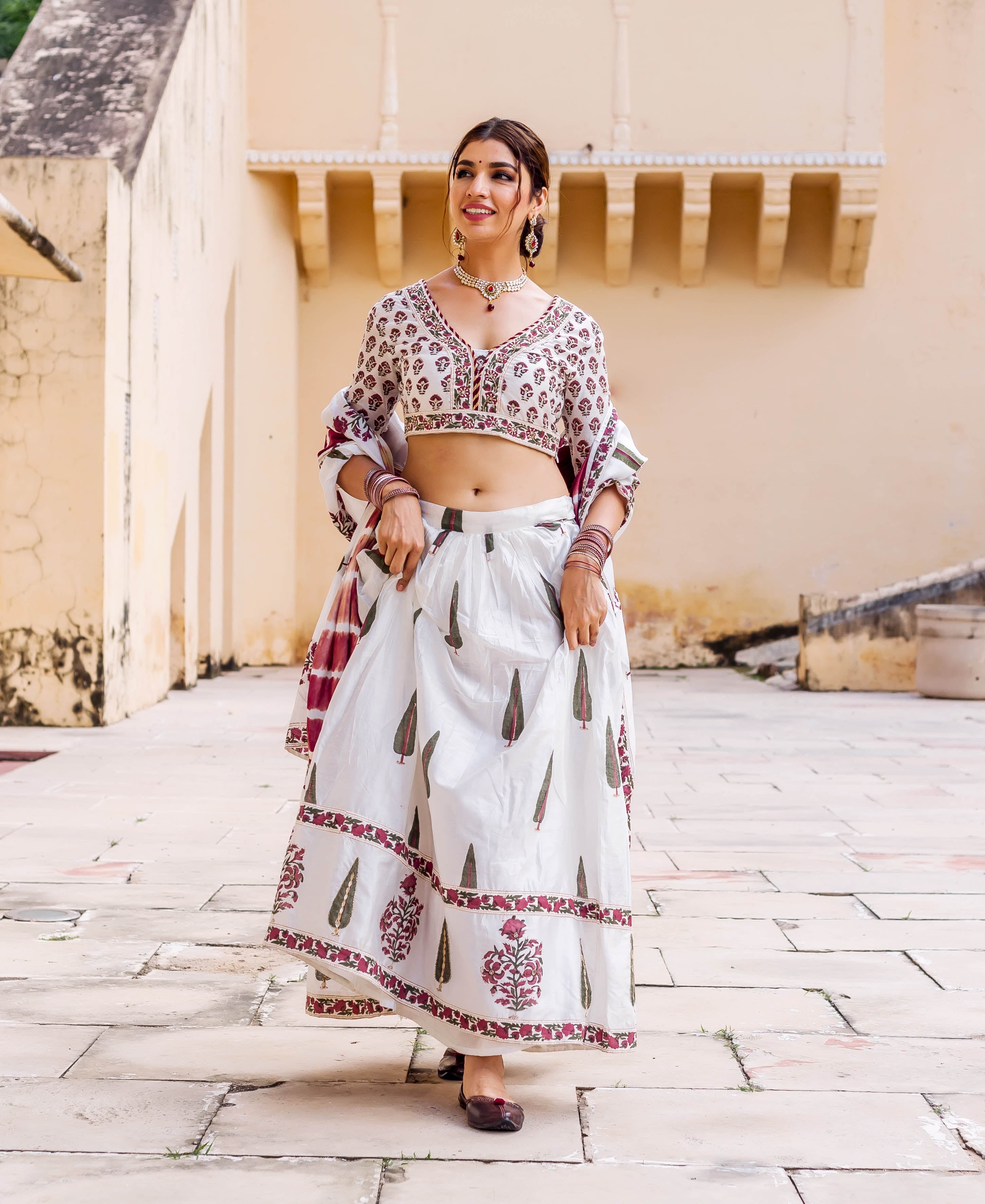 Smiling model in white hand-block printed lehenga set with maroon and green patterns.