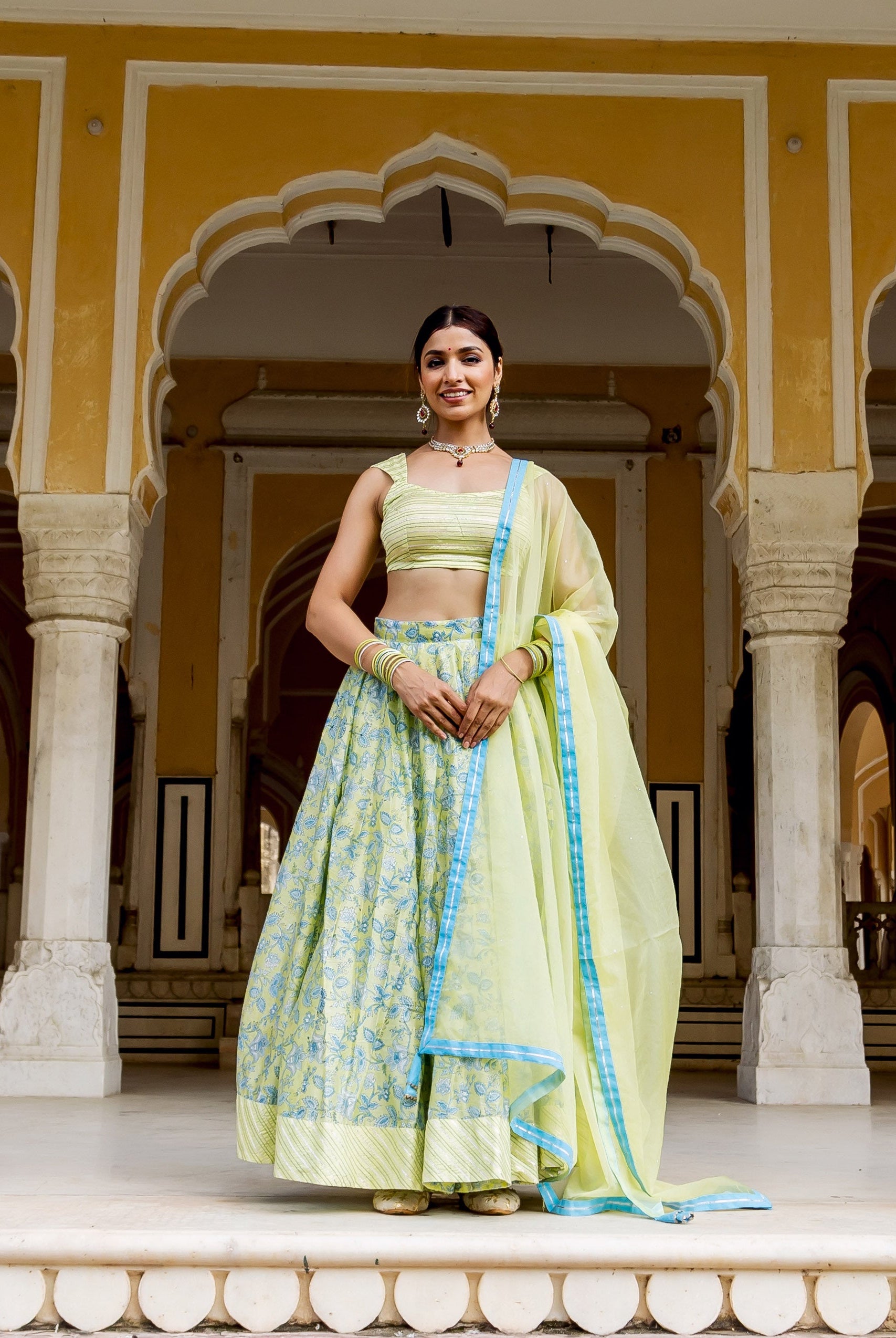 Smiling model in a light green hand block printed lehenga set with blue patterns.