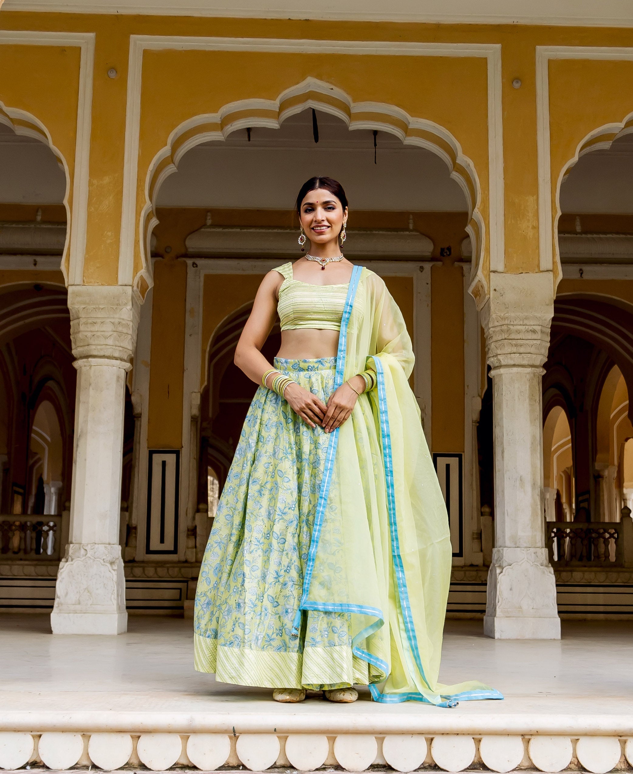 Smiling model in a light green hand block printed lehenga set with blue patterns.