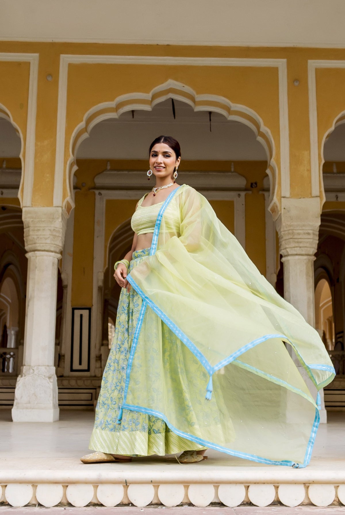 Model in a pale green hand block printed lehenga set with blue accents and flowing dupatta.