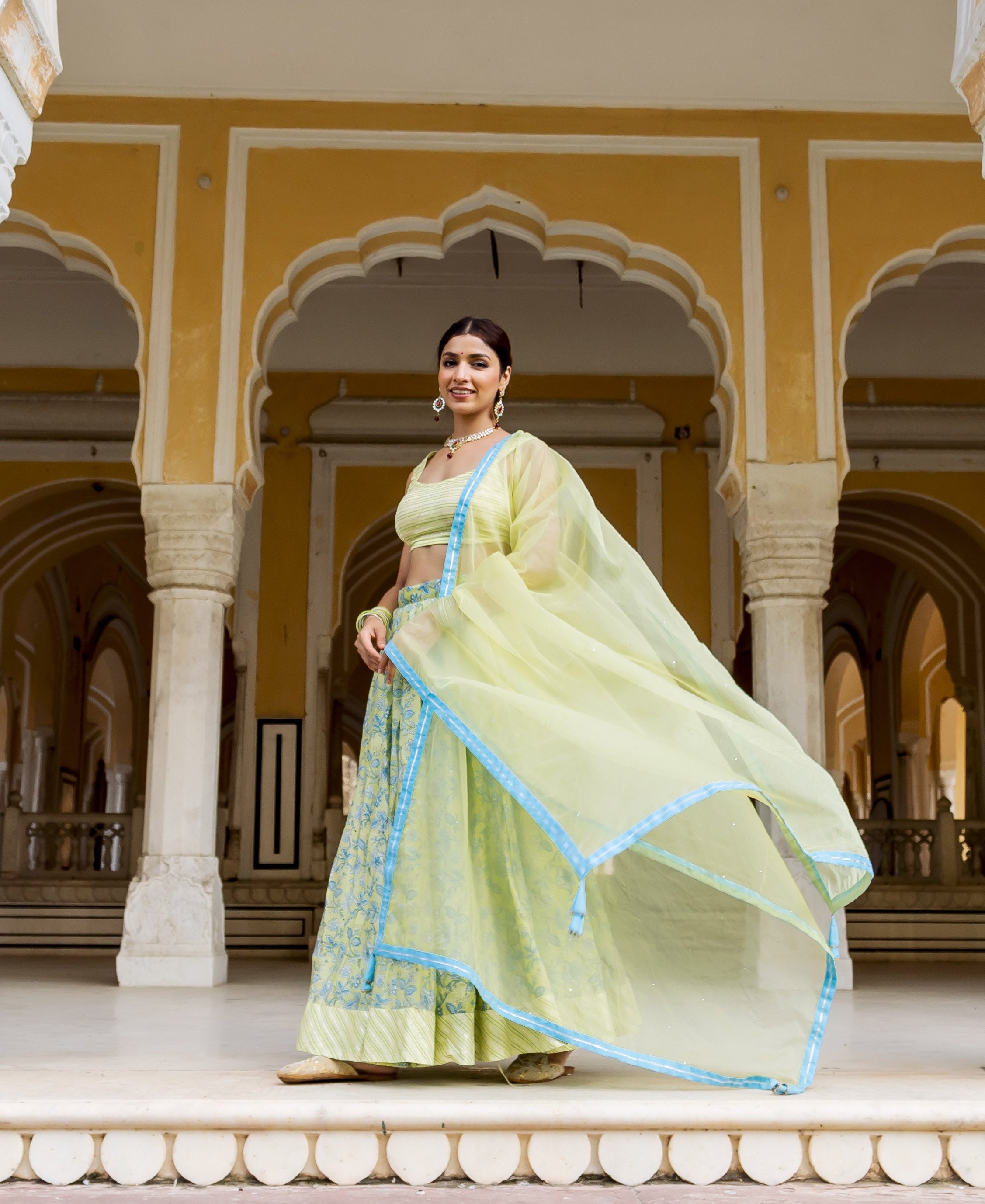 Model in a pale green hand block printed lehenga set with blue accents and flowing dupatta.