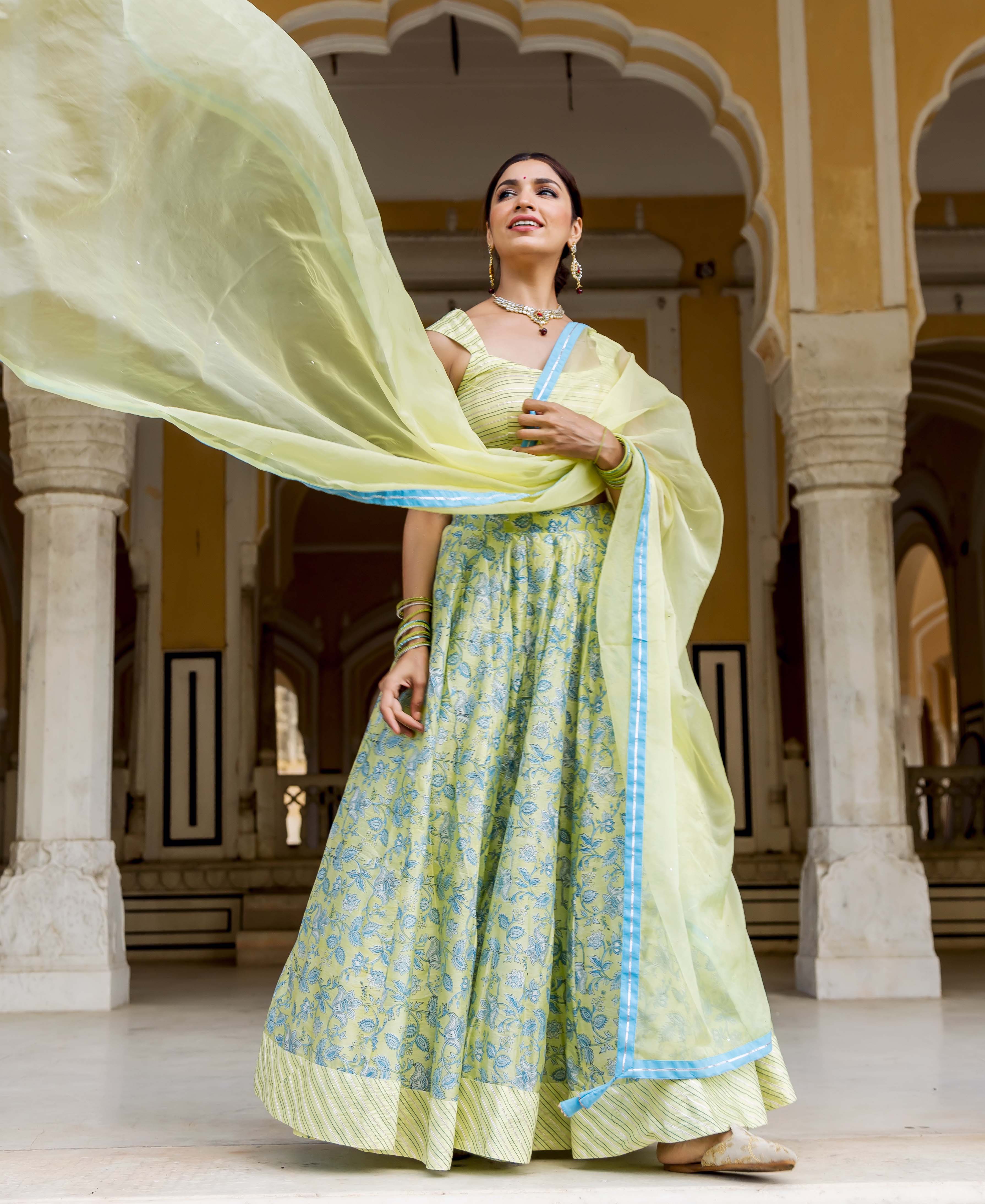 Model wearing lime green hand-block printed lehenga set with blue floral patterns and flowing dupatta.