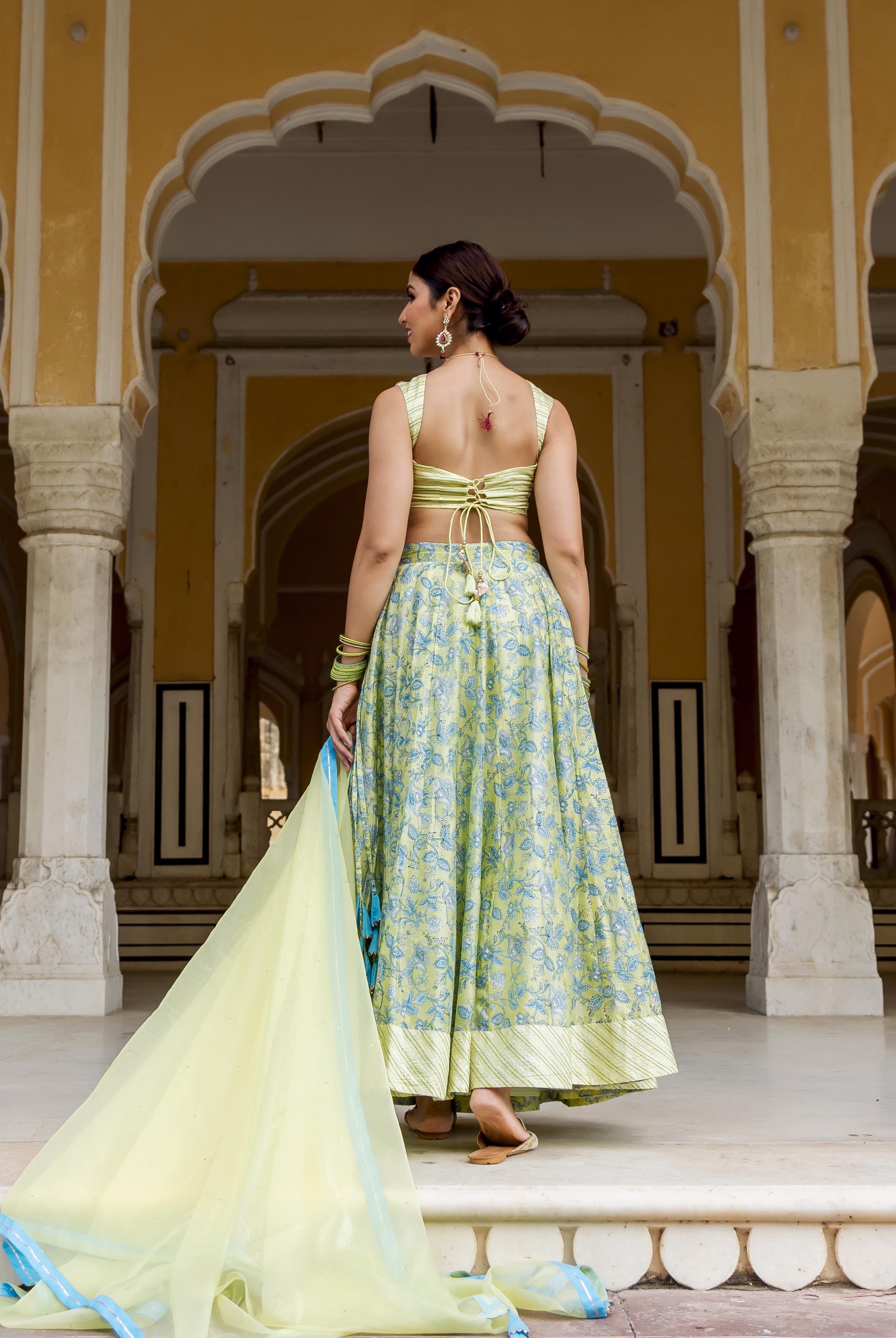 Back view of model in light green, blue hand-block printed lehenga set with tie-up choli.