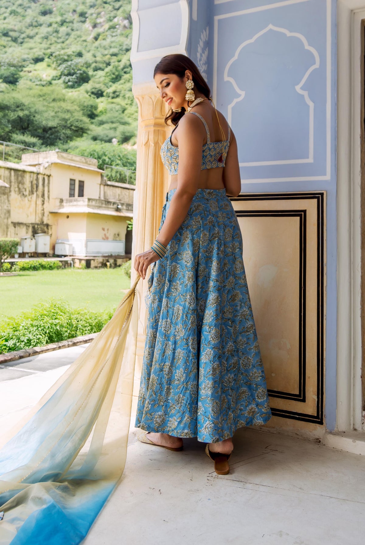 Three-quarter back view of model in blue floral hand-block printed lehenga with flowing dupatta.
