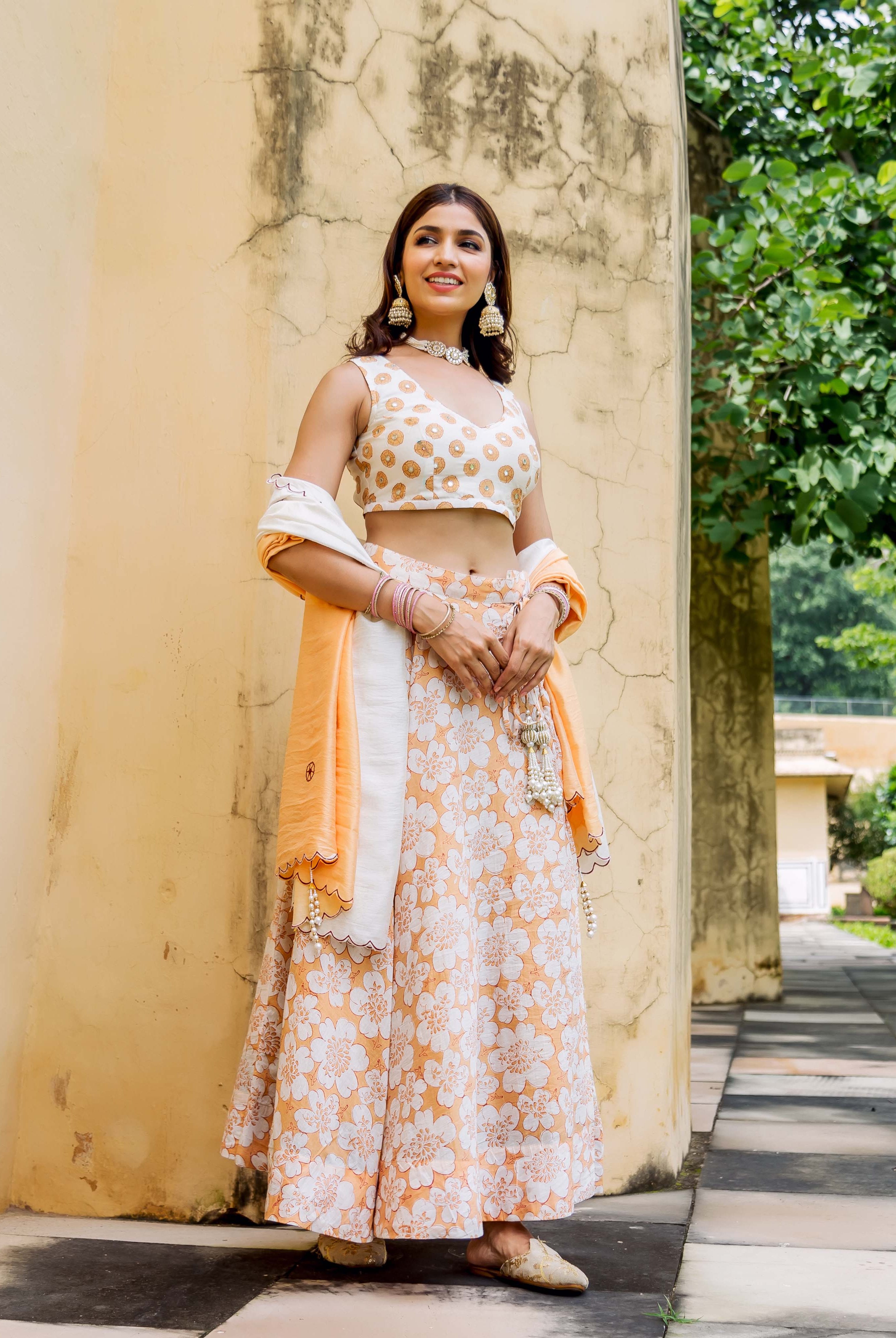 Model wearing an off-white and orange embroidered crop top and floral block print lehenga set.