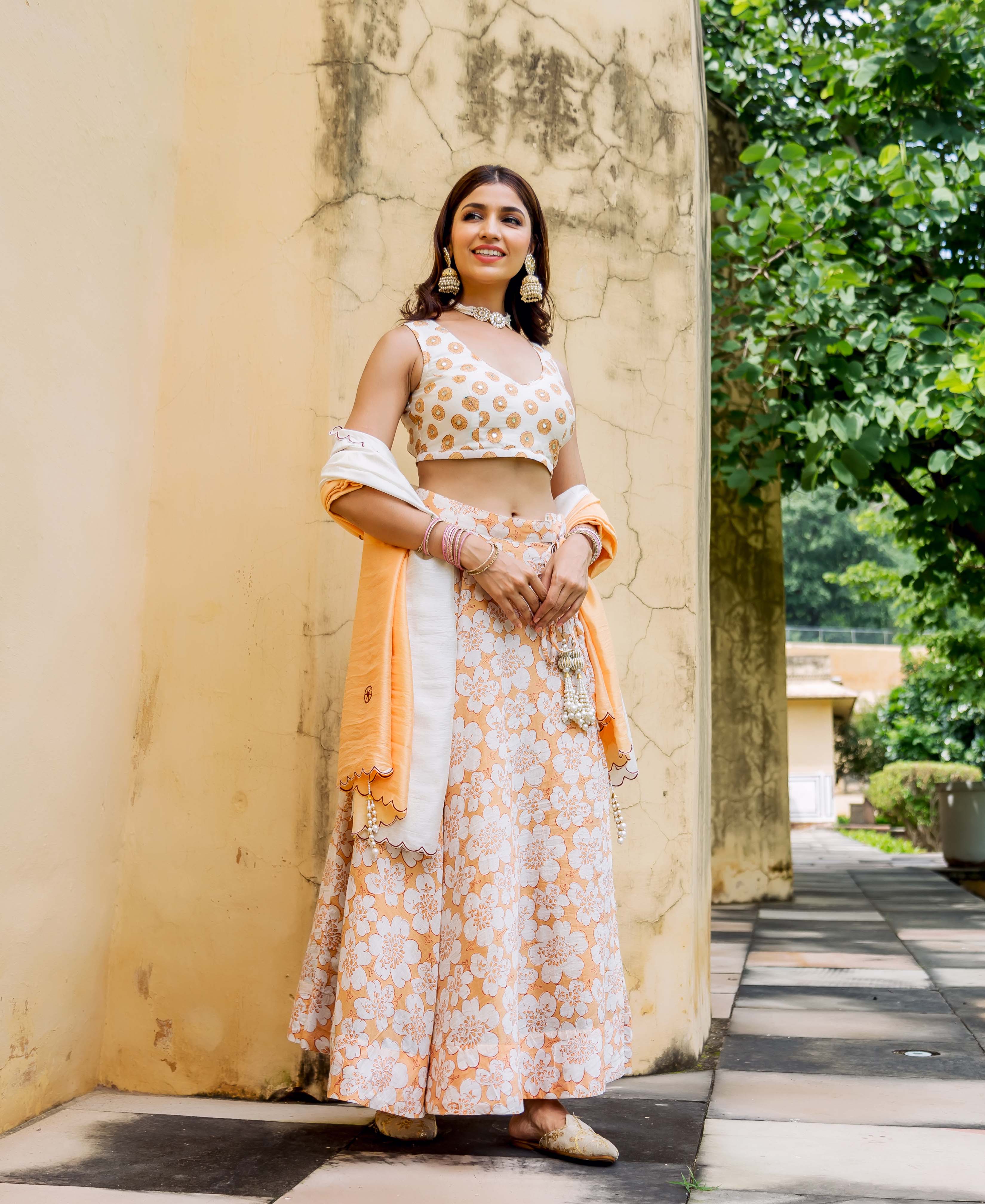 Model wearing an off-white and orange embroidered crop top and floral block print lehenga set.