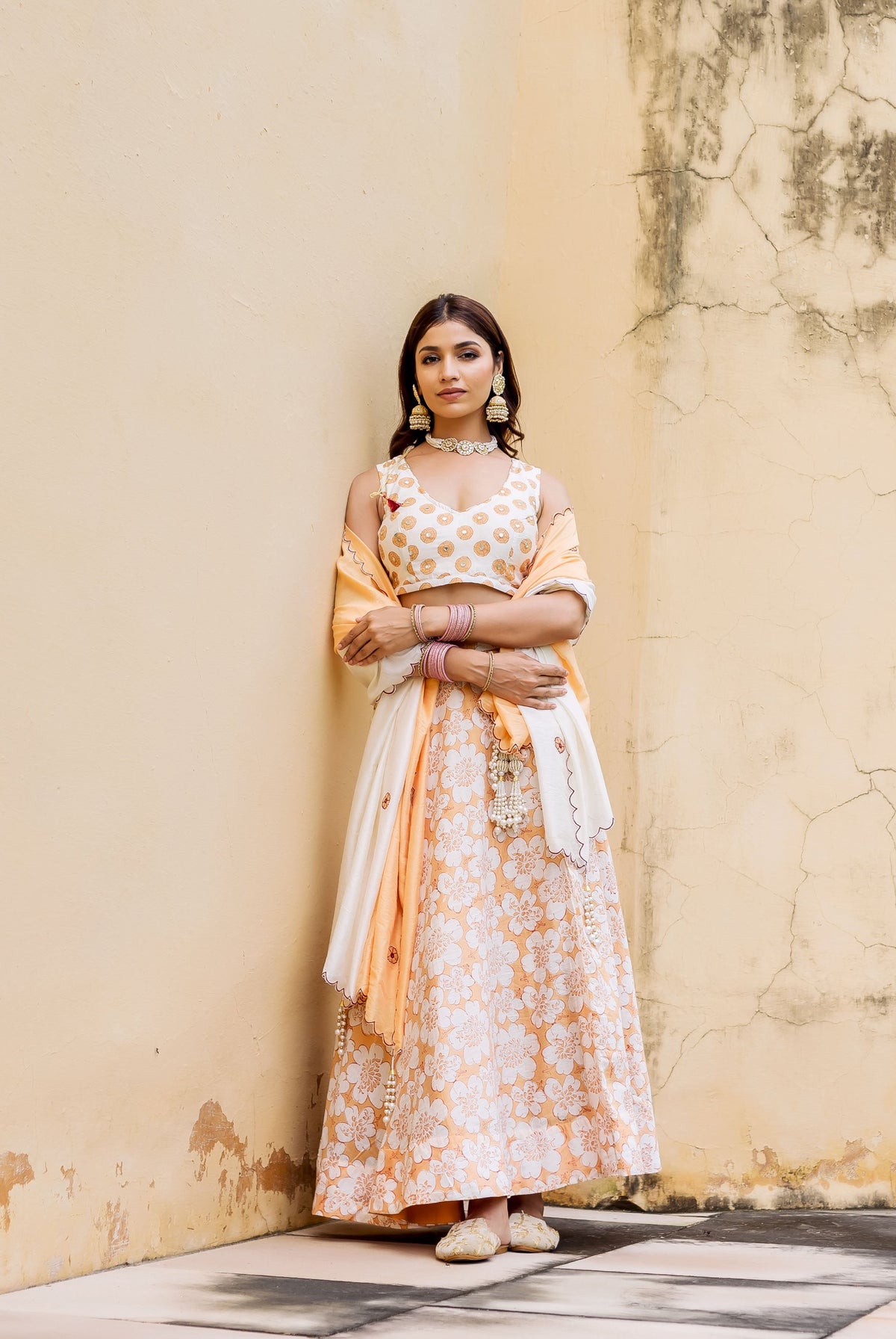 Model wearing off-white and peach block printed floral lehenga set, with gold dotted choli.