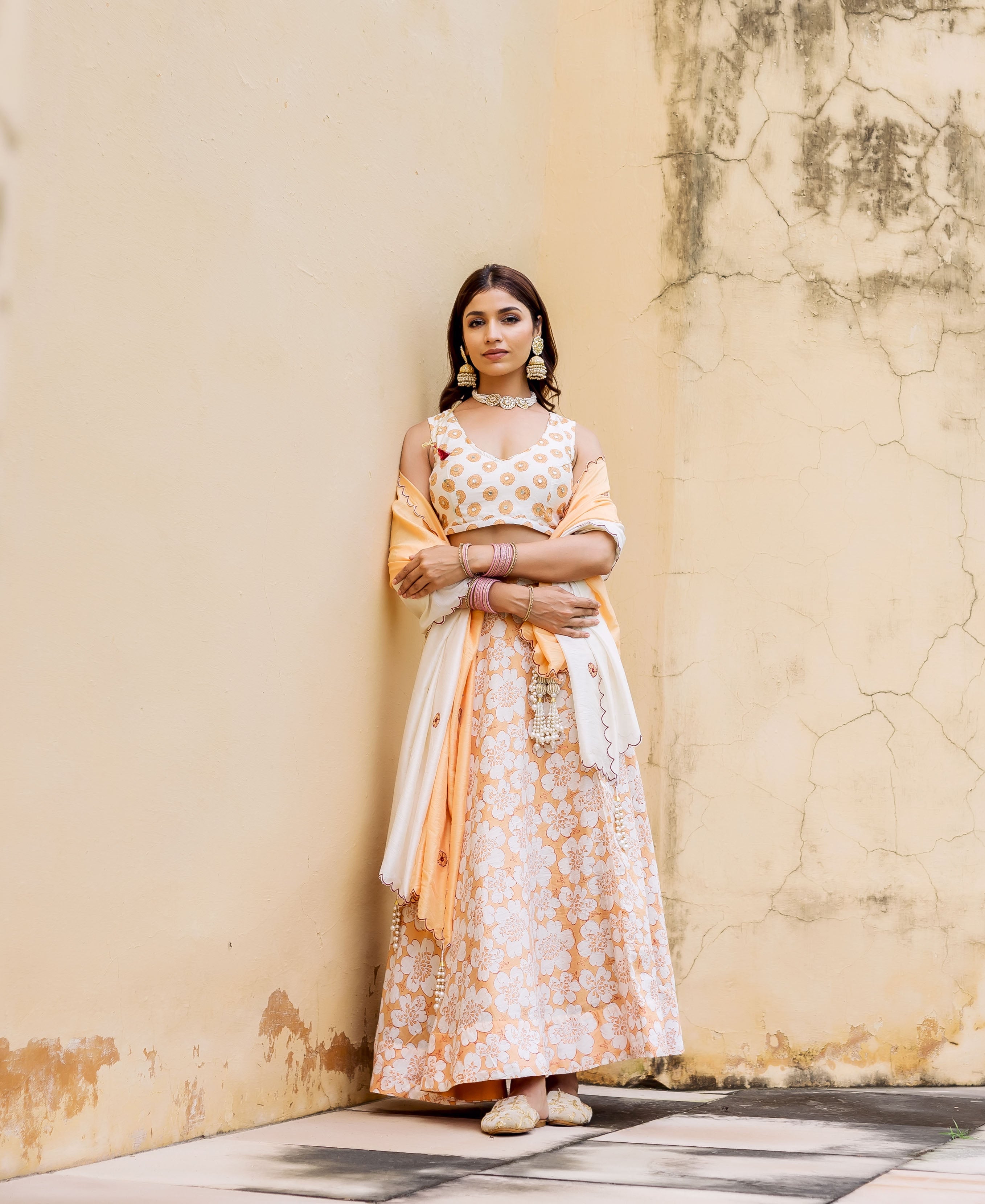 Model wearing off-white and peach block printed floral lehenga set, with gold dotted choli.