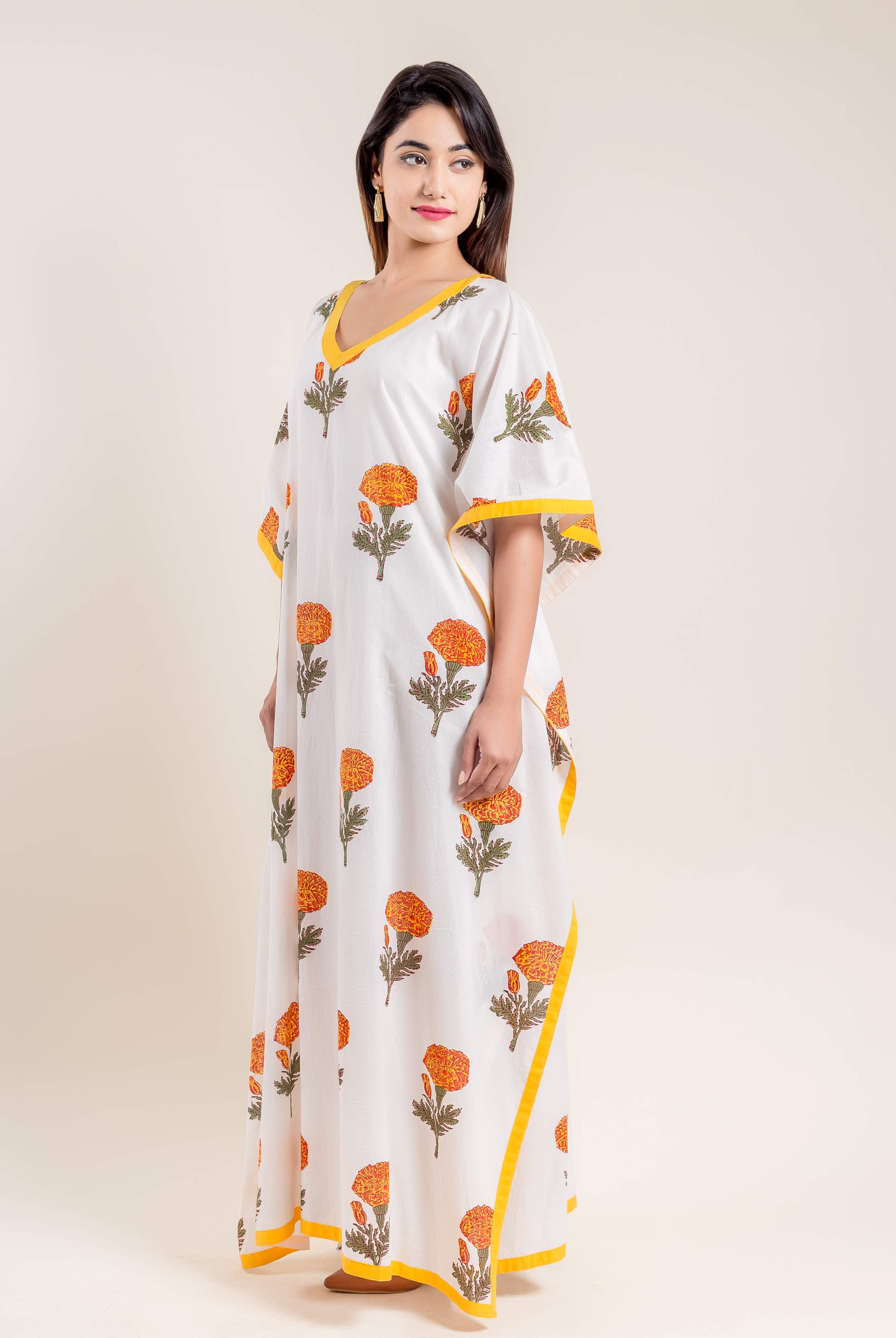 Model wearing white hand block printed V-neck kaftan with marigold print and yellow trim.