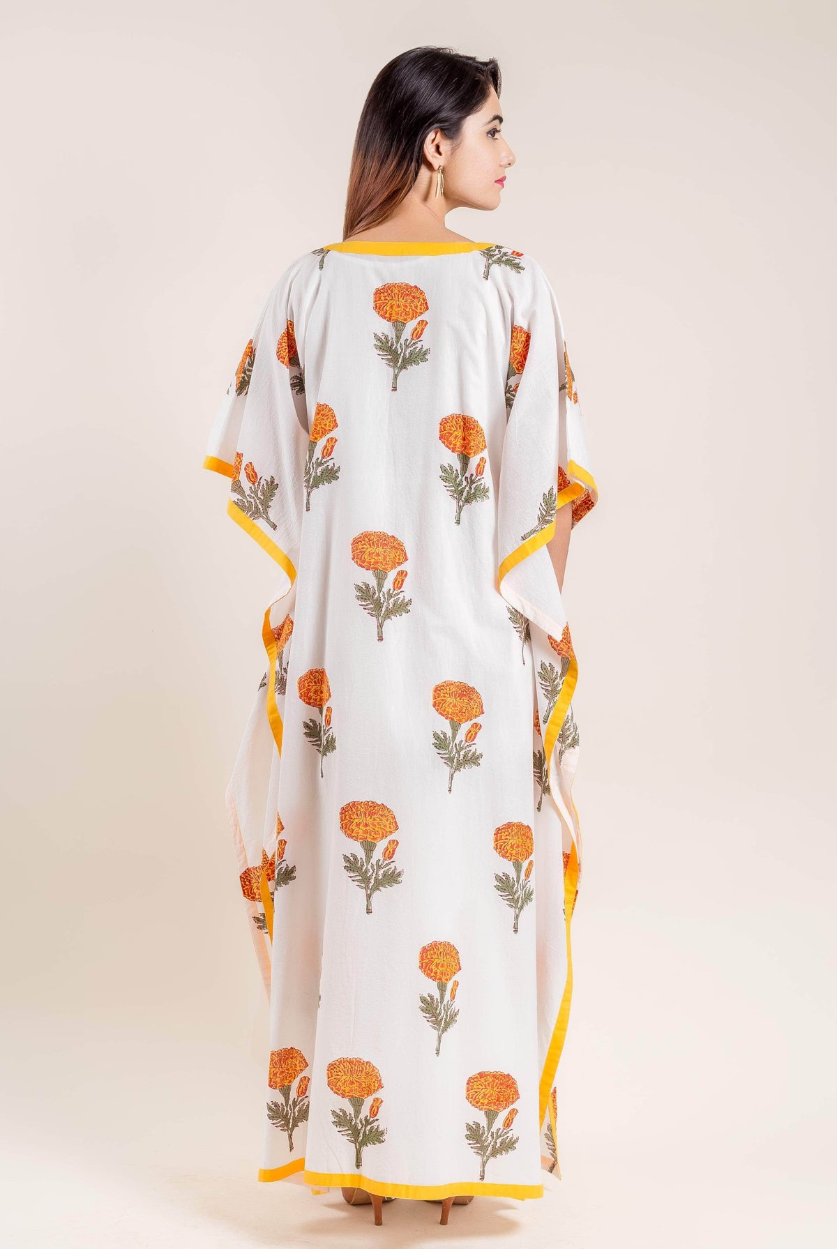 Back view of model wearing white kaftan with orange block printed flowers and yellow trim.