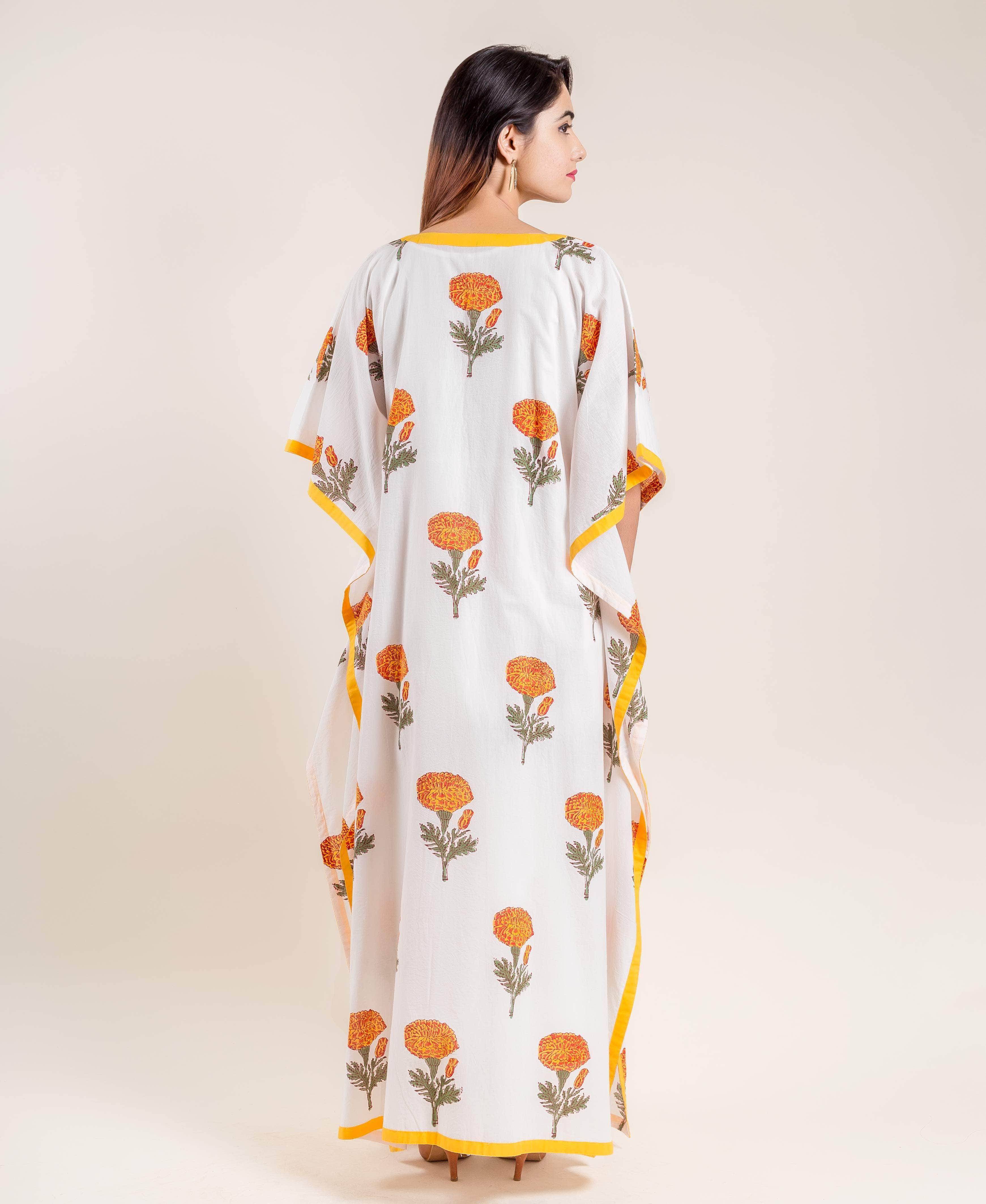 Back view of model wearing white kaftan with orange block printed flowers and yellow trim.