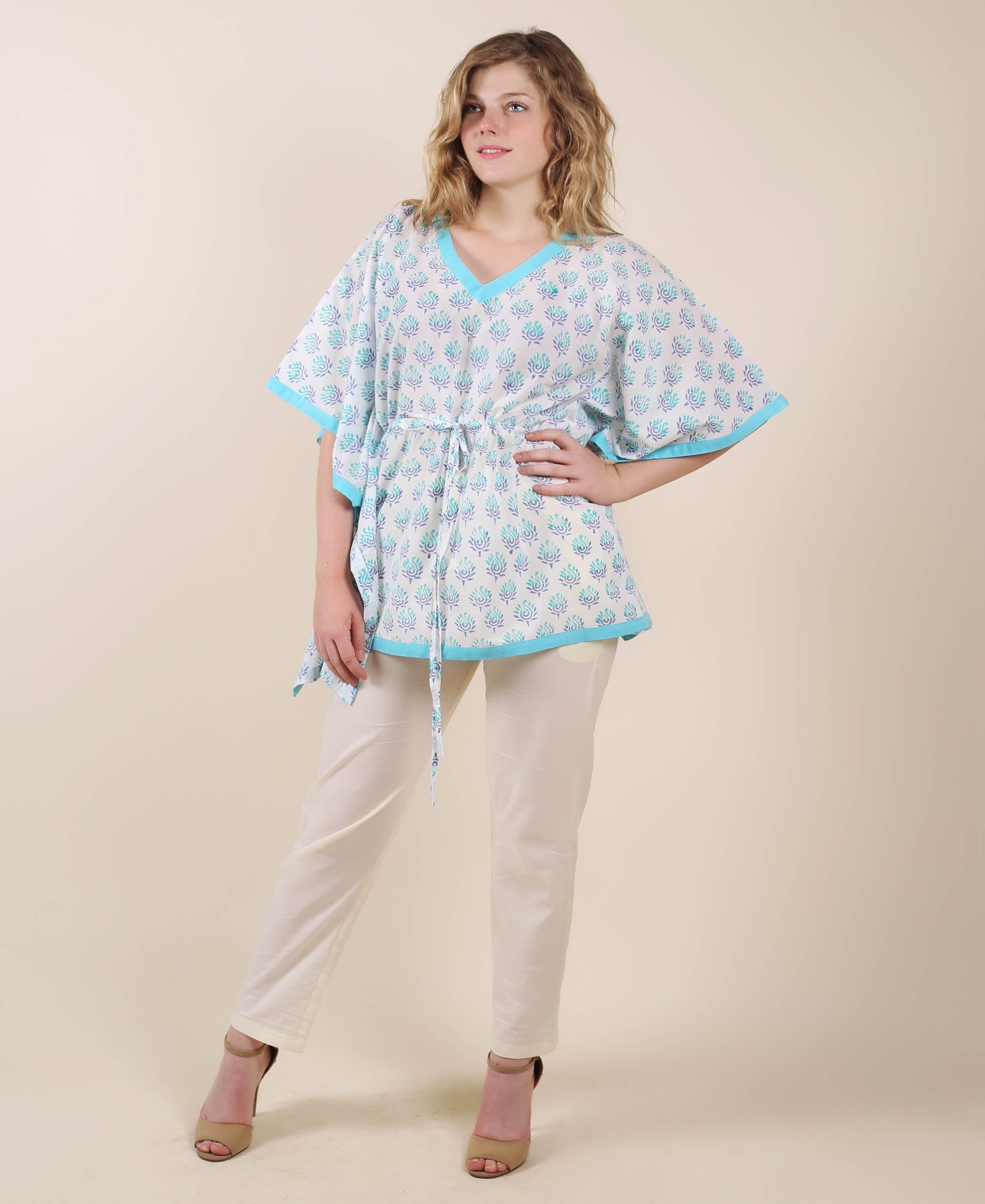 Full-length model wears white kaftan top with aqua ethnic block print, drawstring, and cream trousers.