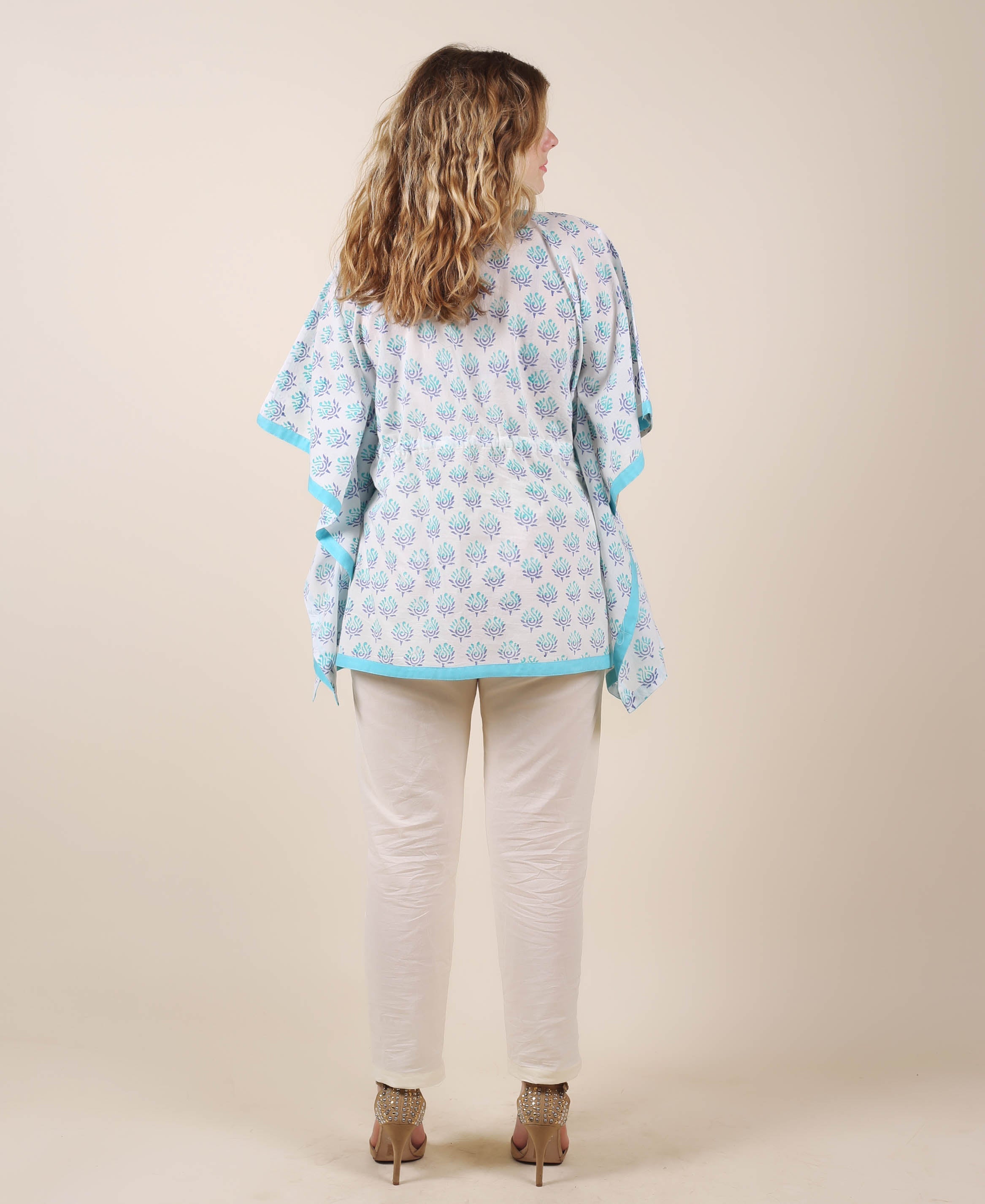 Back view of model in white kaftan with aqua blue leafy print, white trousers.