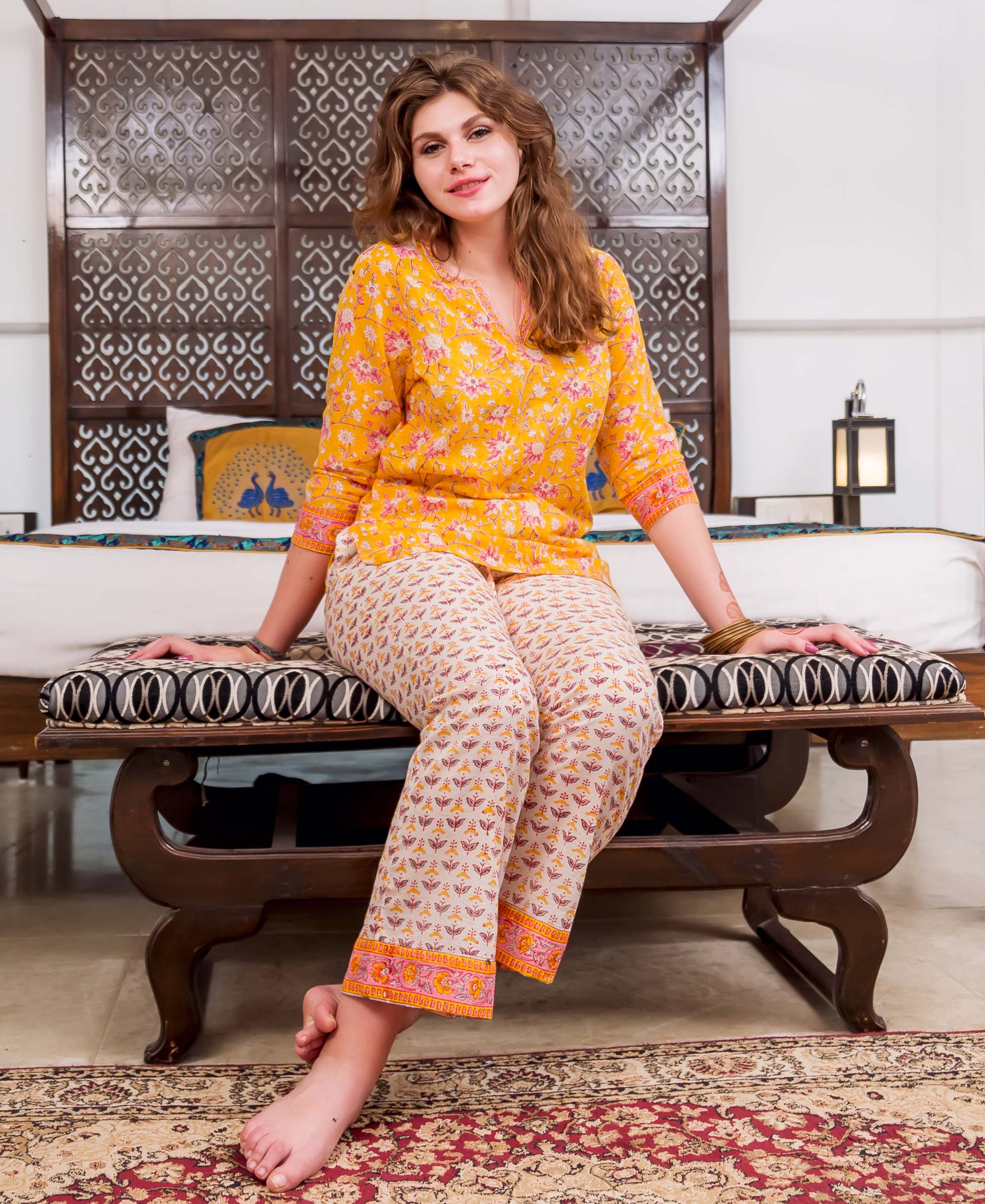 Woman wearing vibrant yellow and white block printed pajama set with floral patterns and pink accents.