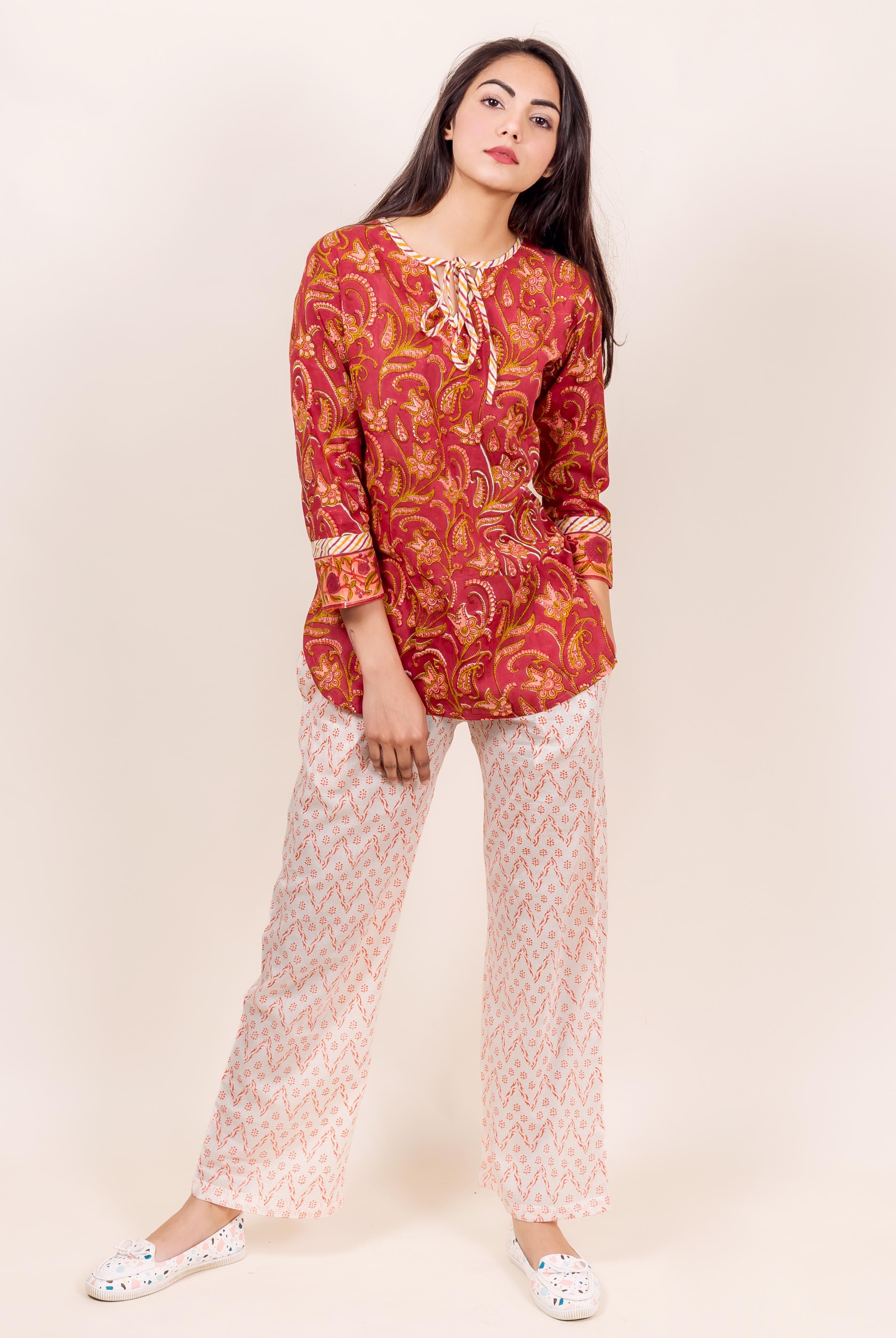 Front view of a model wearing a rust-red paisley top and white geometric block printed pajamas.
