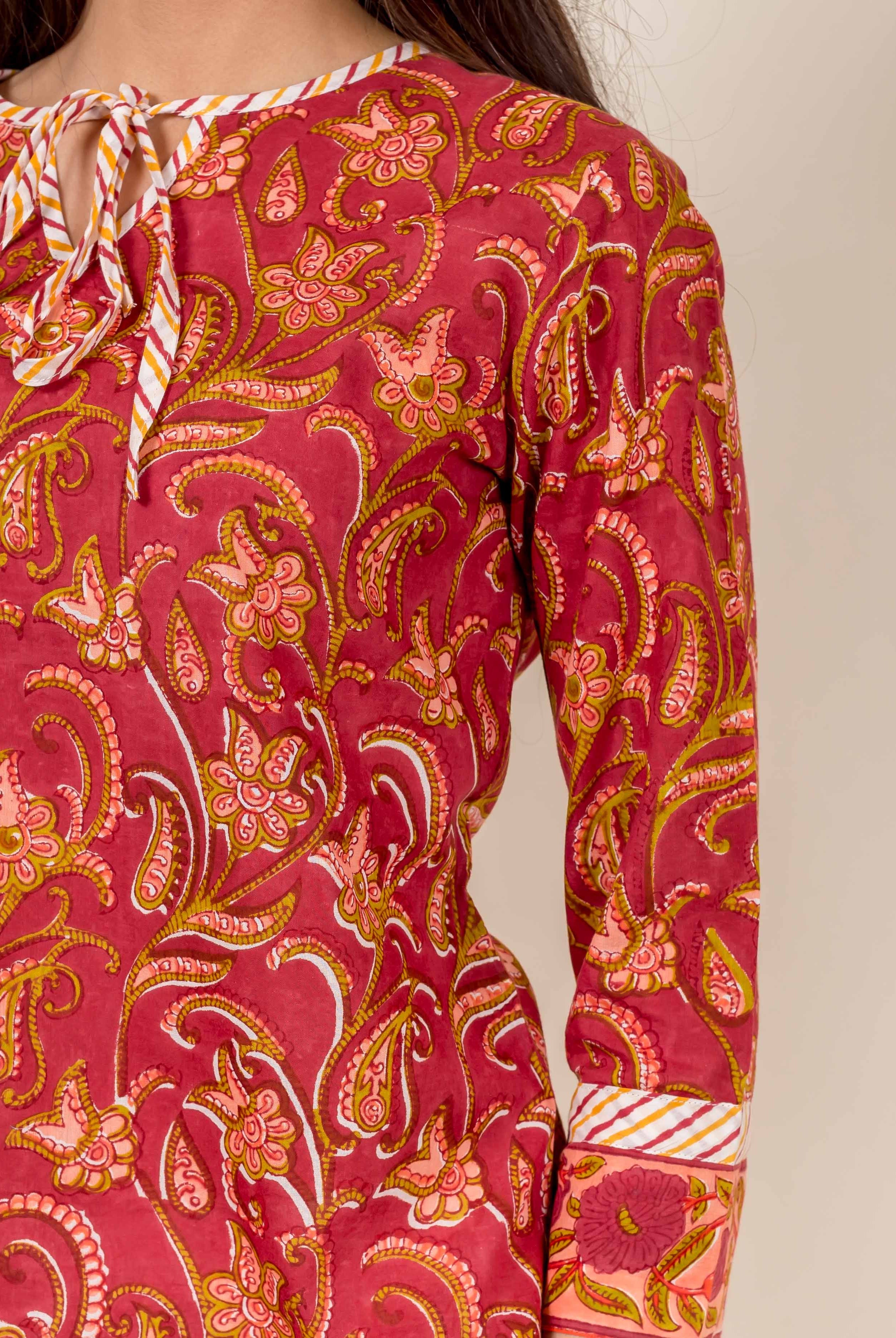 Close-up of model wearing rust block-printed top with floral, paisley, and striped tie-neck.