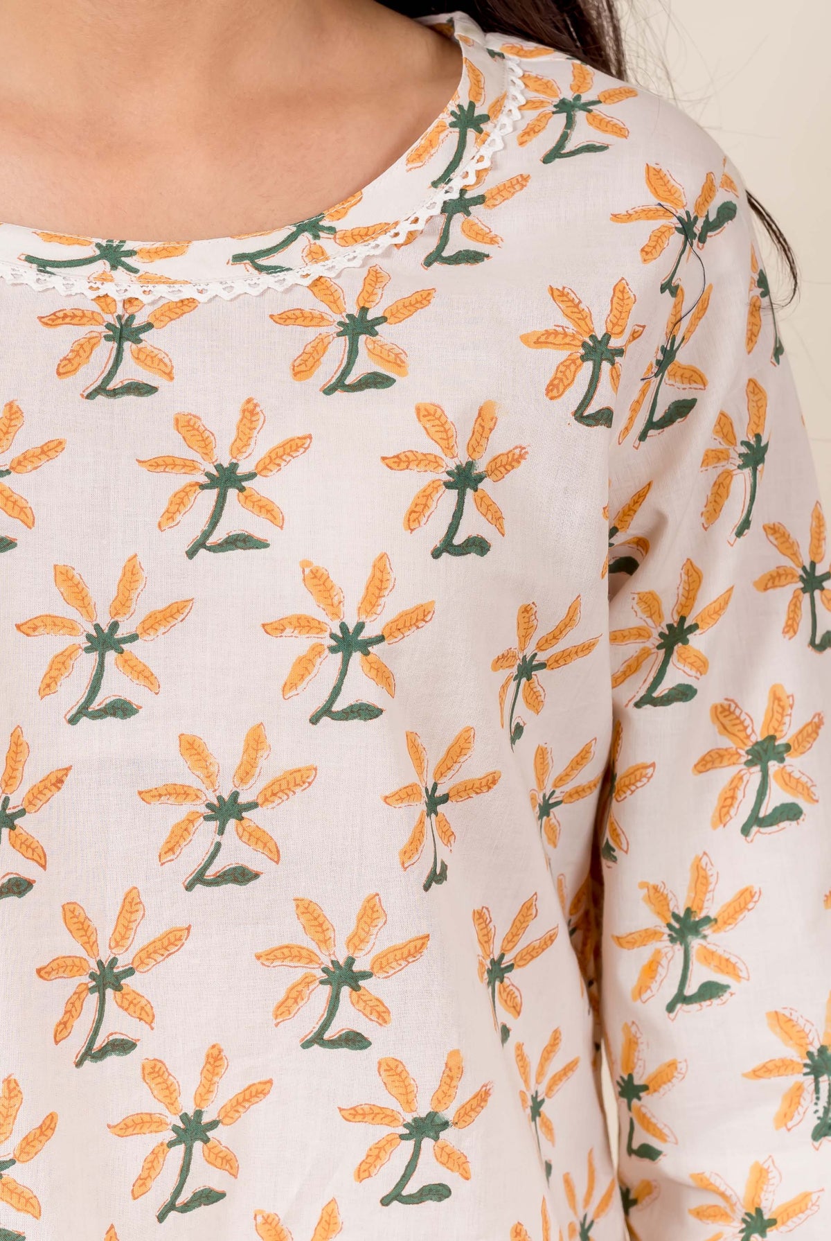 Close-up of model wearing beige block-printed top with orange-green floral patterns and lace neckline.