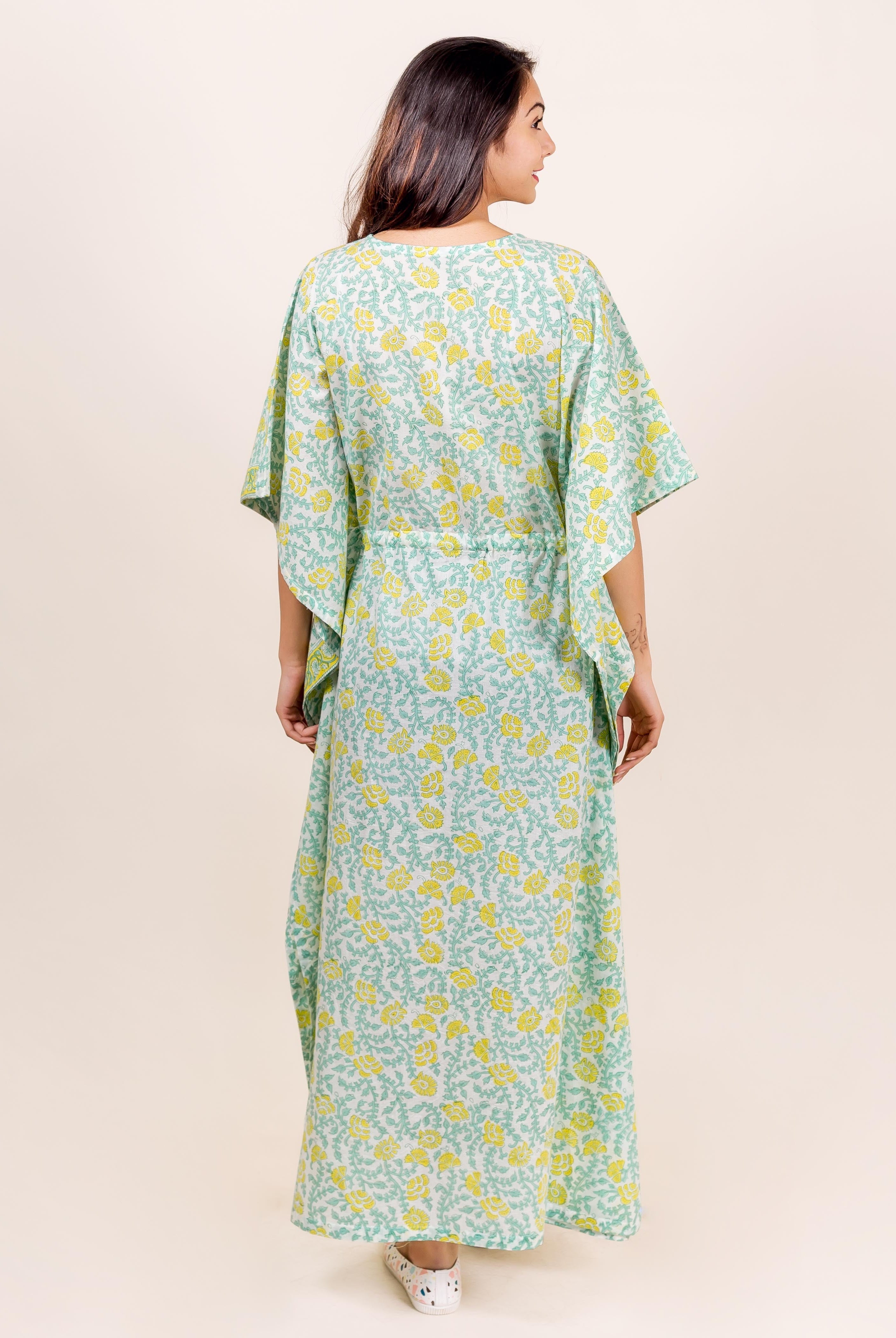 Back view of model wearing full-length mint green kaftan with yellow floral block print.