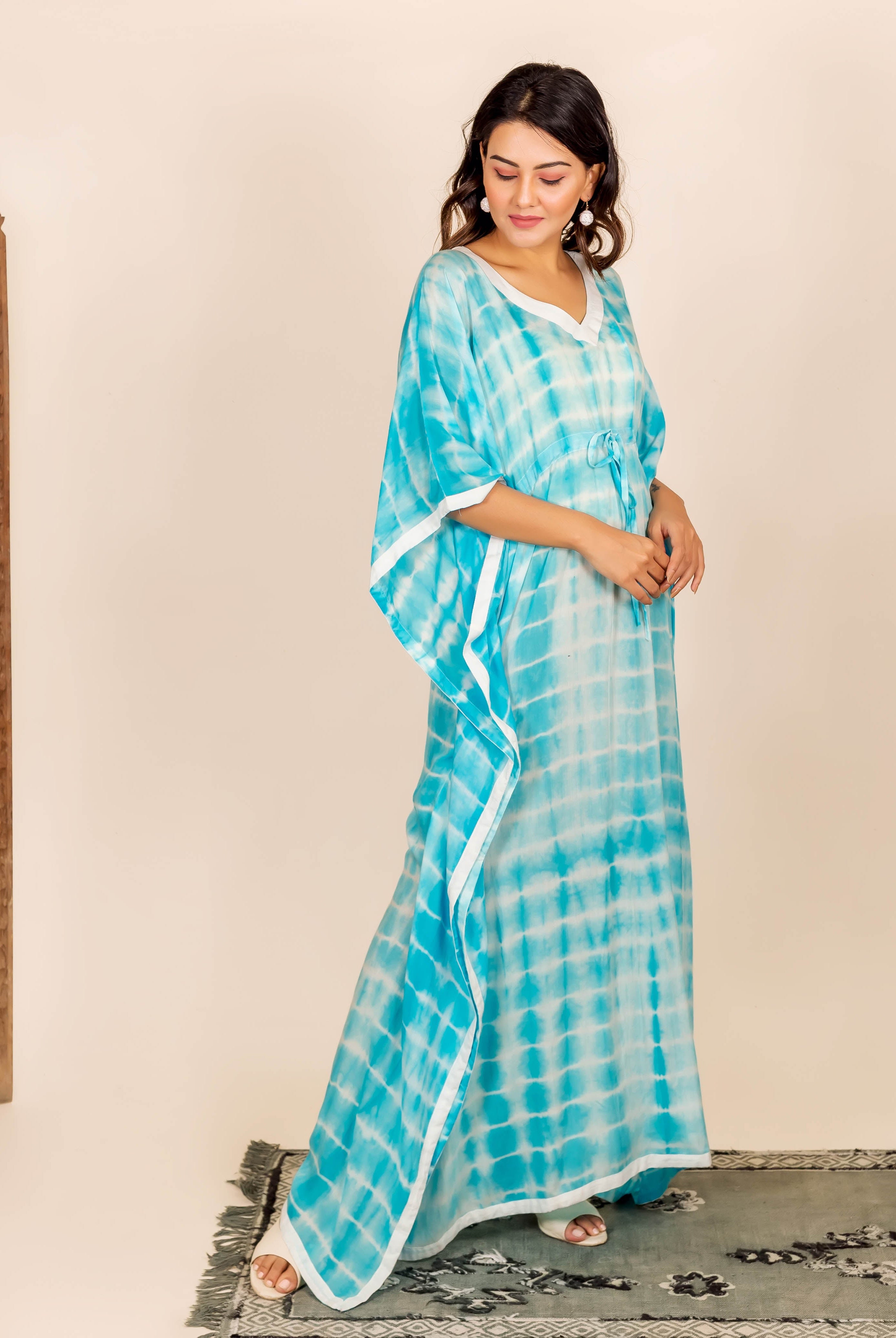 Woman wearing aqua and white tie-dye kaftan with adjustable waist line and white trim.