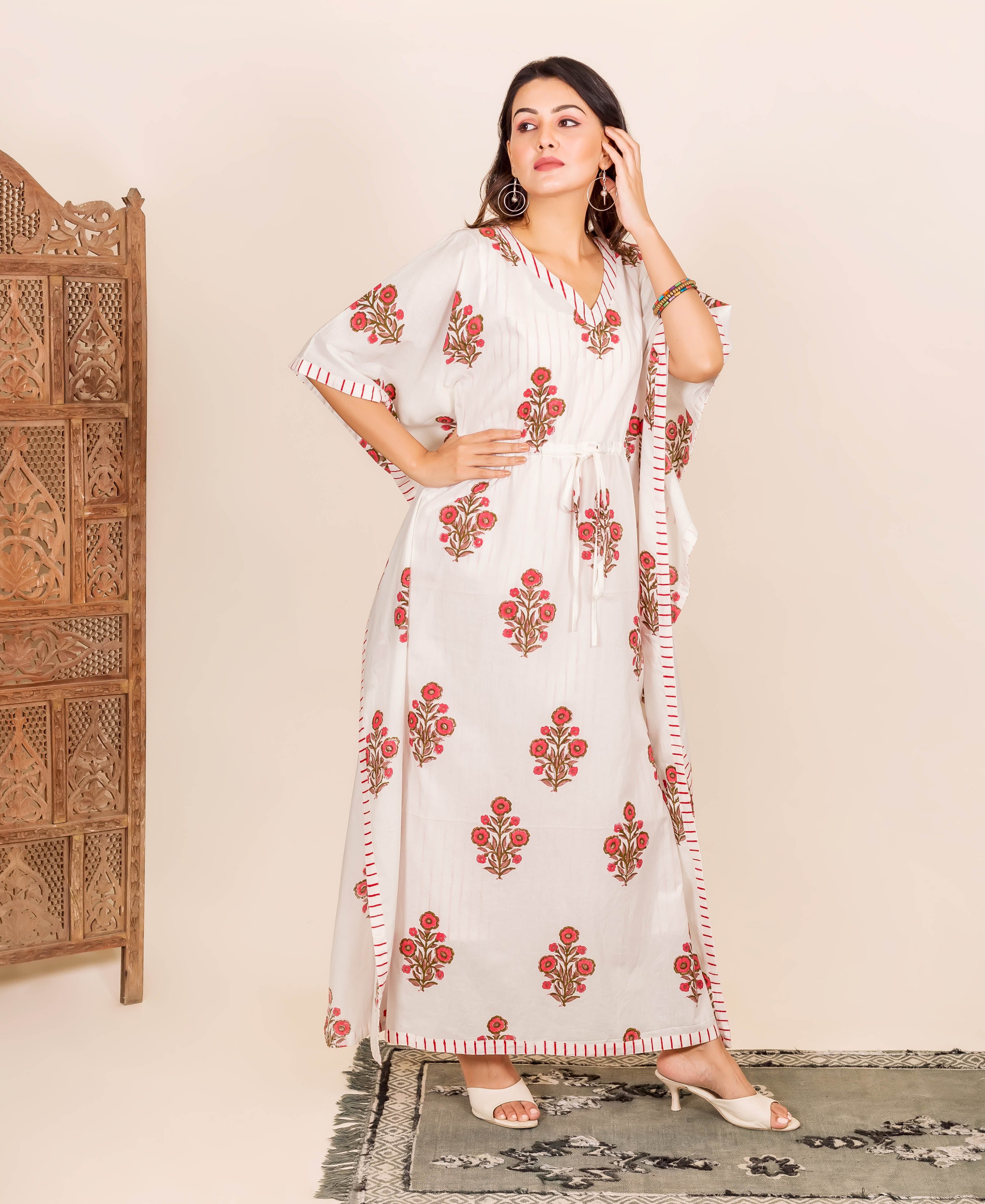 A woman in a white kaftan with red floral print, standing on a rug.