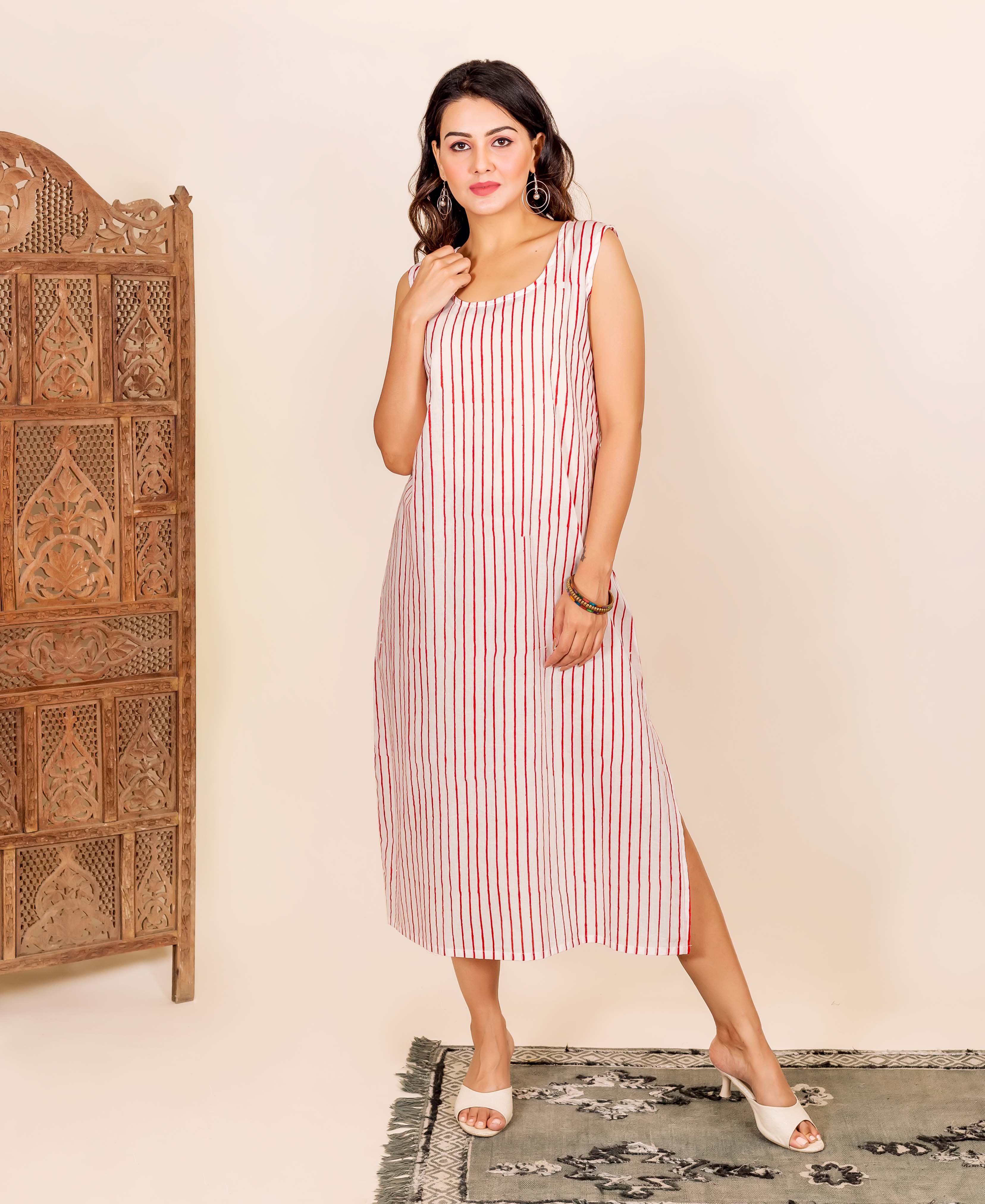 A woman wearing a white kaftan with red stripes, standing on a rug.